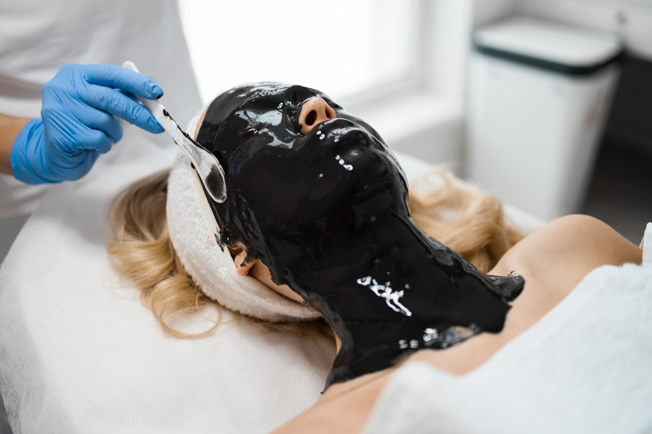 Person receiving black facial mask treatment