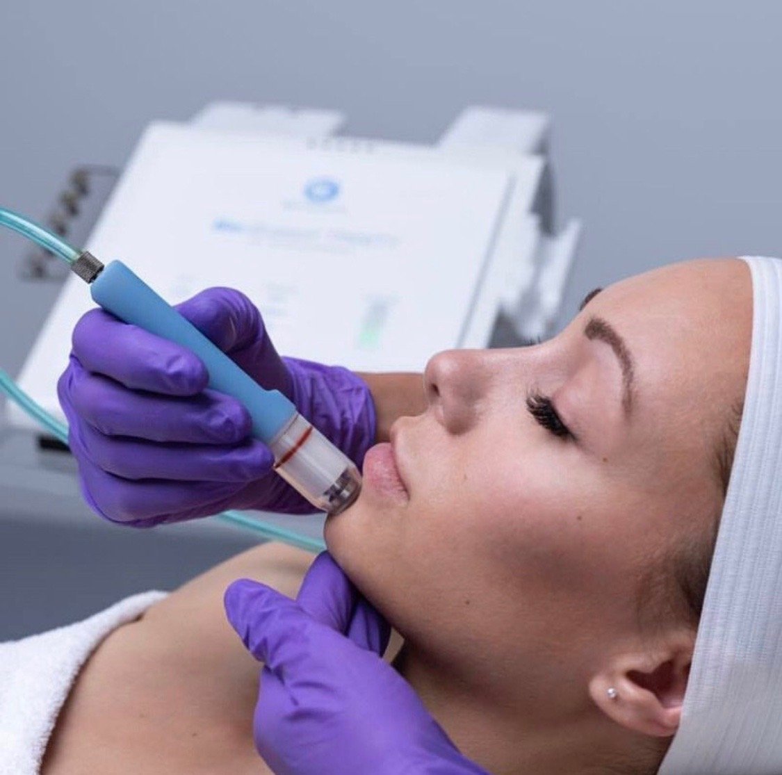 Person receiving facial treatment with a handheld device, wearing purple gloves.