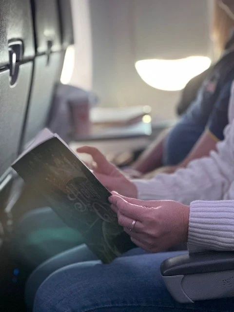 Author sitting at book signing table with a large poster promoting her book titled 'Holly and Oak, Season One' behind her. There are copies of her book on the table.
