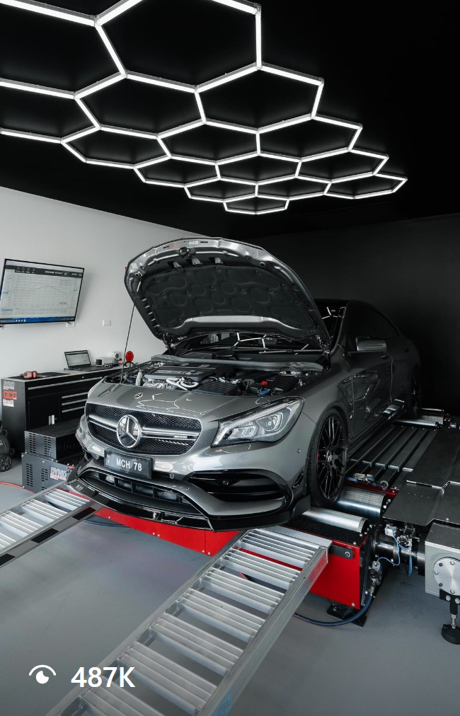 A thumbnail of a video of a gray Mercedes-Benz car with its hood open on a dynamometer testing machine in an automotive laboratory with contemporary hexagonal LED ceiling lights. The video has 487k views on the Instagram UI.
