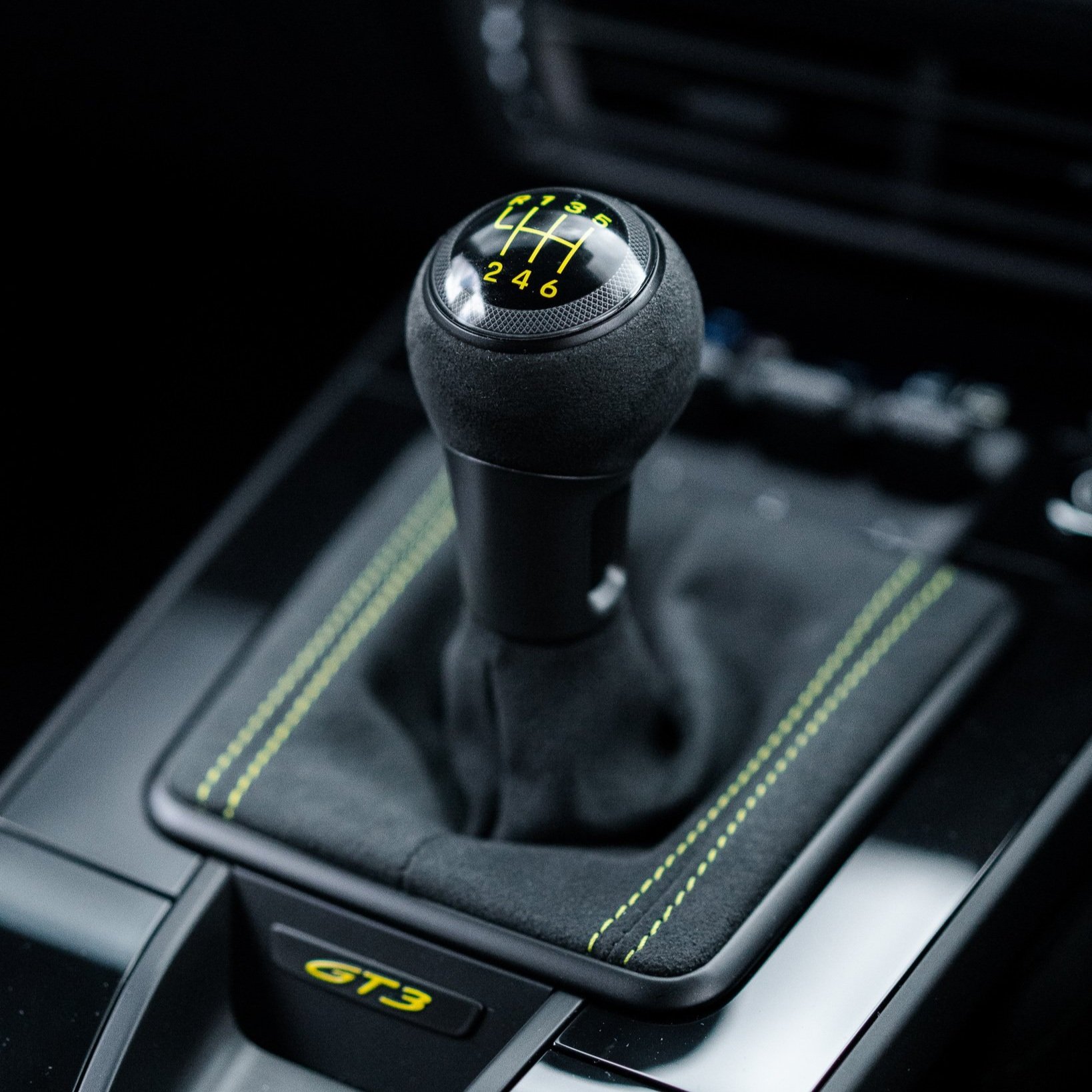 Close-up of a manual gear shift knob in a GT3 car with yellow stitching.