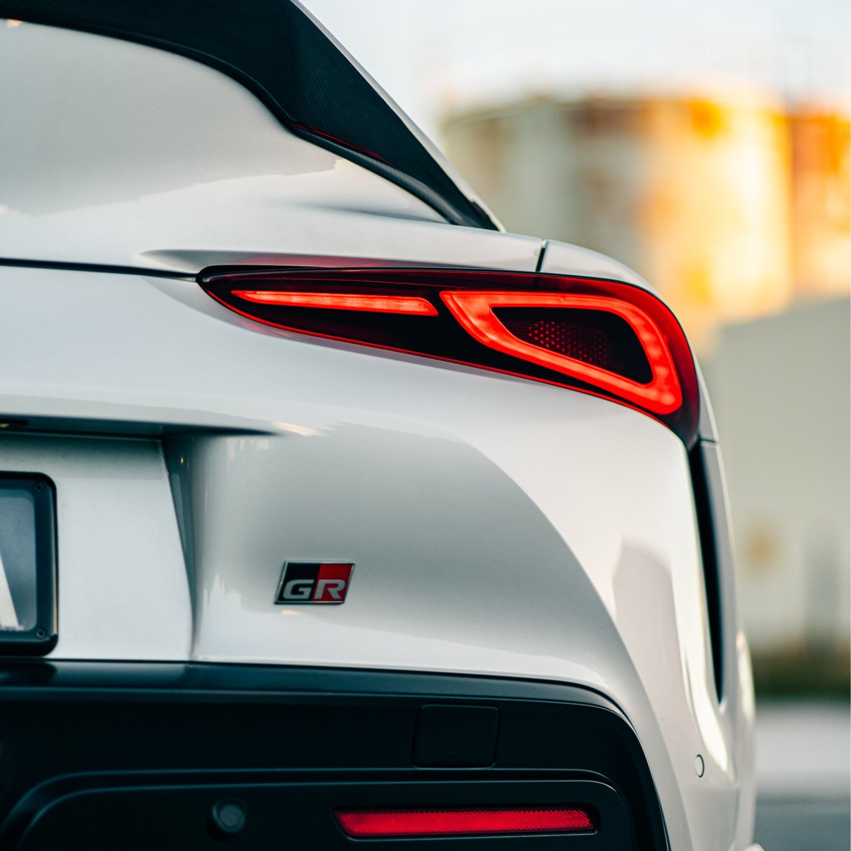 Close-up of the rear of a white sports car with a red GR emblem and illuminated taillights.