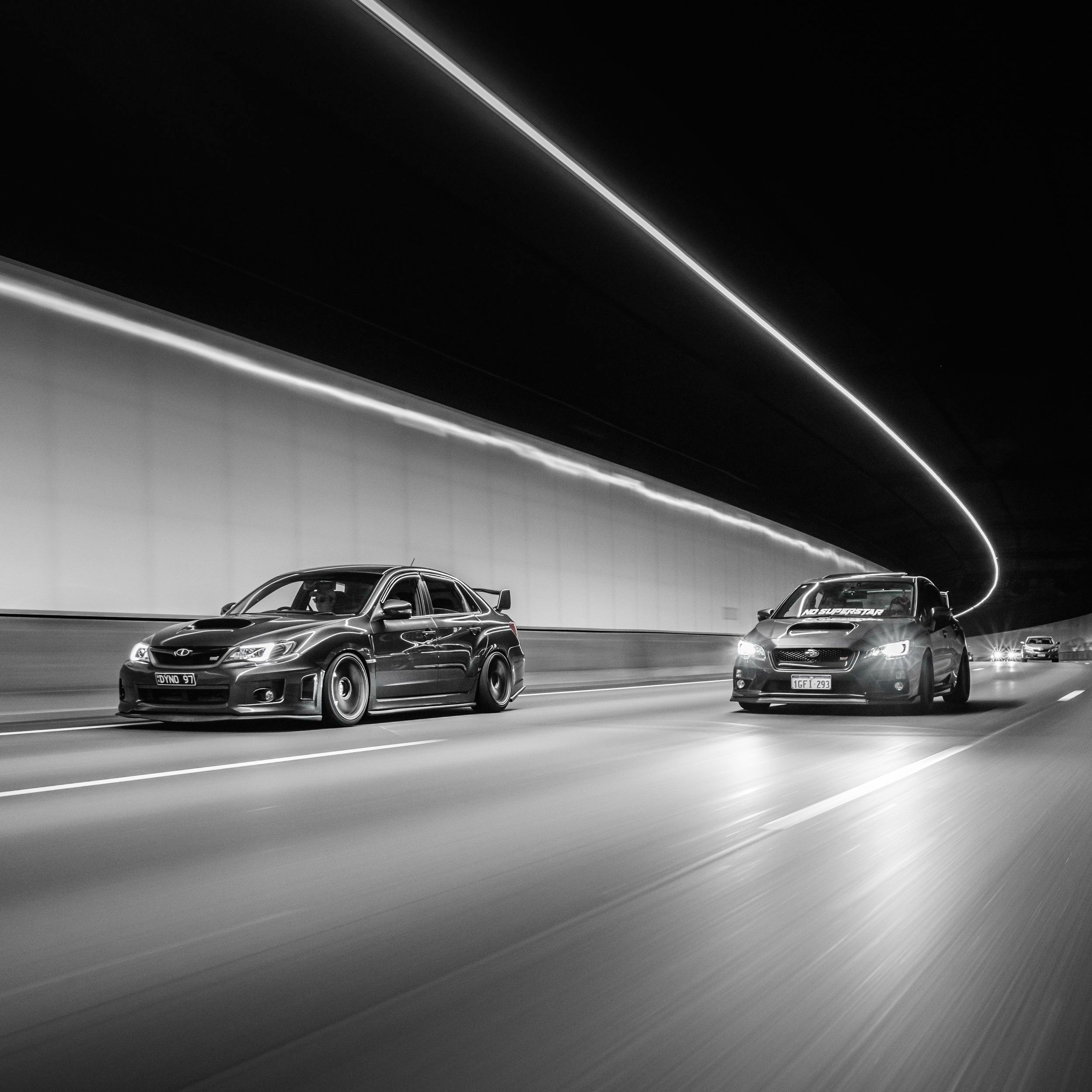 Two cars driving side by side in a tunnel with a sleek, modern design, captured in black and white.