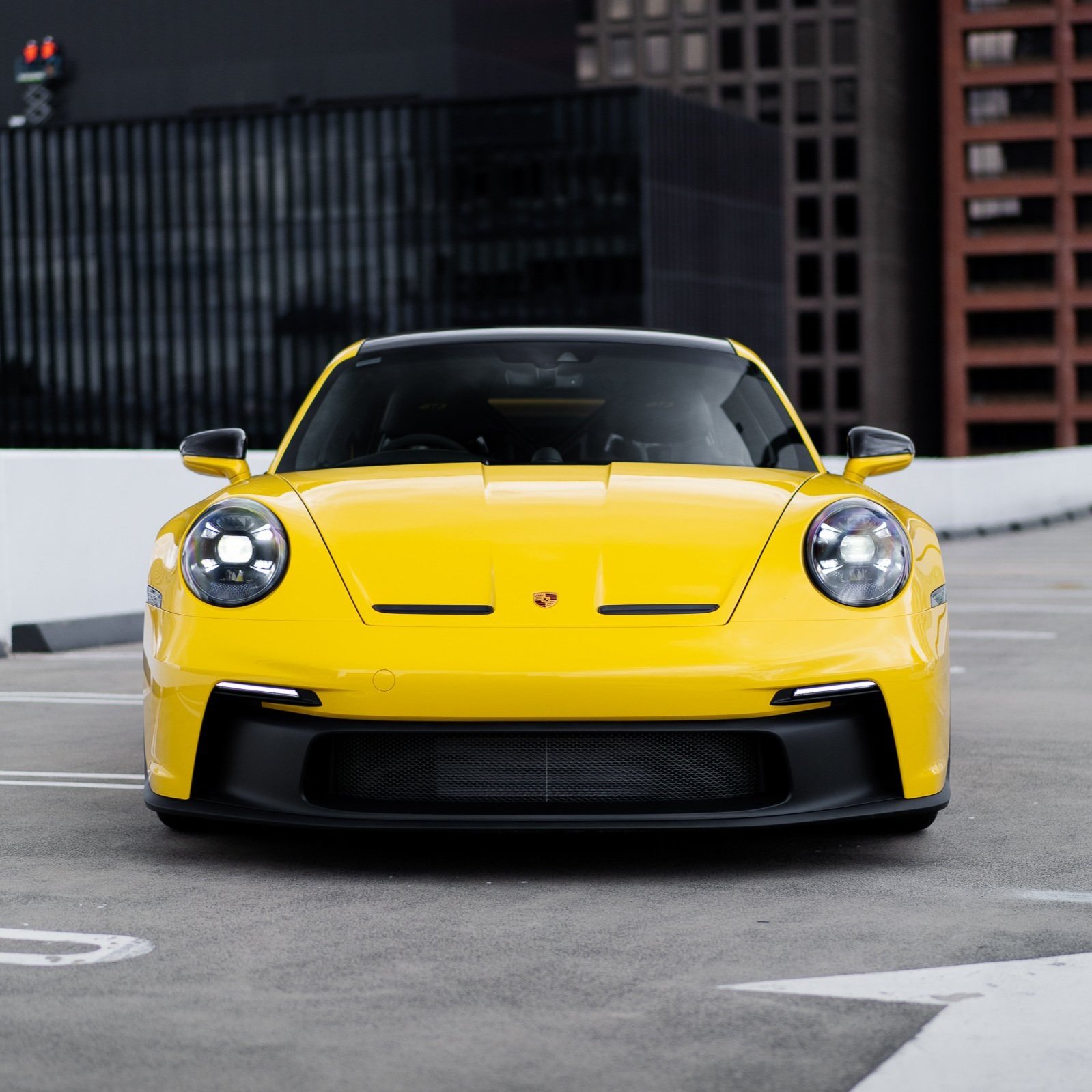 Front view of a yellow sports car parked in an urban setting.