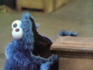 Cookie Monster from Sesame Street peering hungrily over a table, about to devour everything in sight