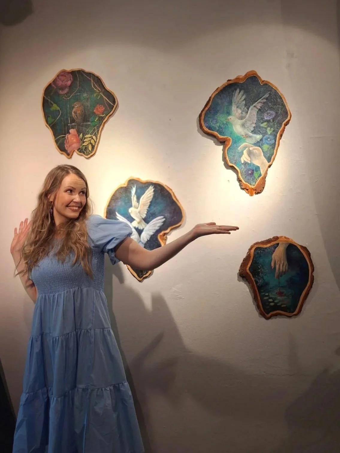 Jonna Jokikunnas beside her figurative paintings on naturally shaped wood.