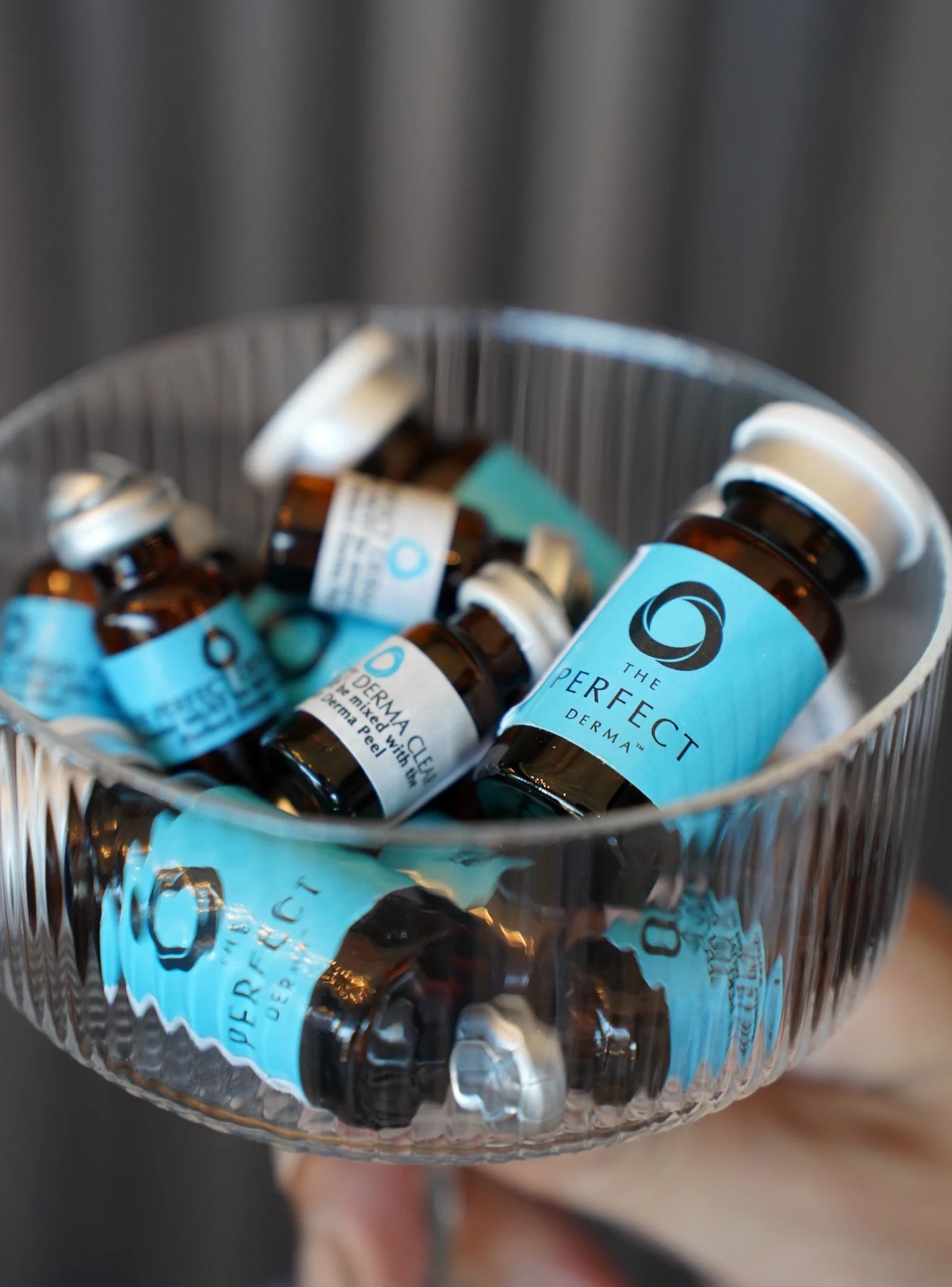 Glass bowl filled with small brown bottles labeled 'The Perfect Derma Peel' with blue labels.