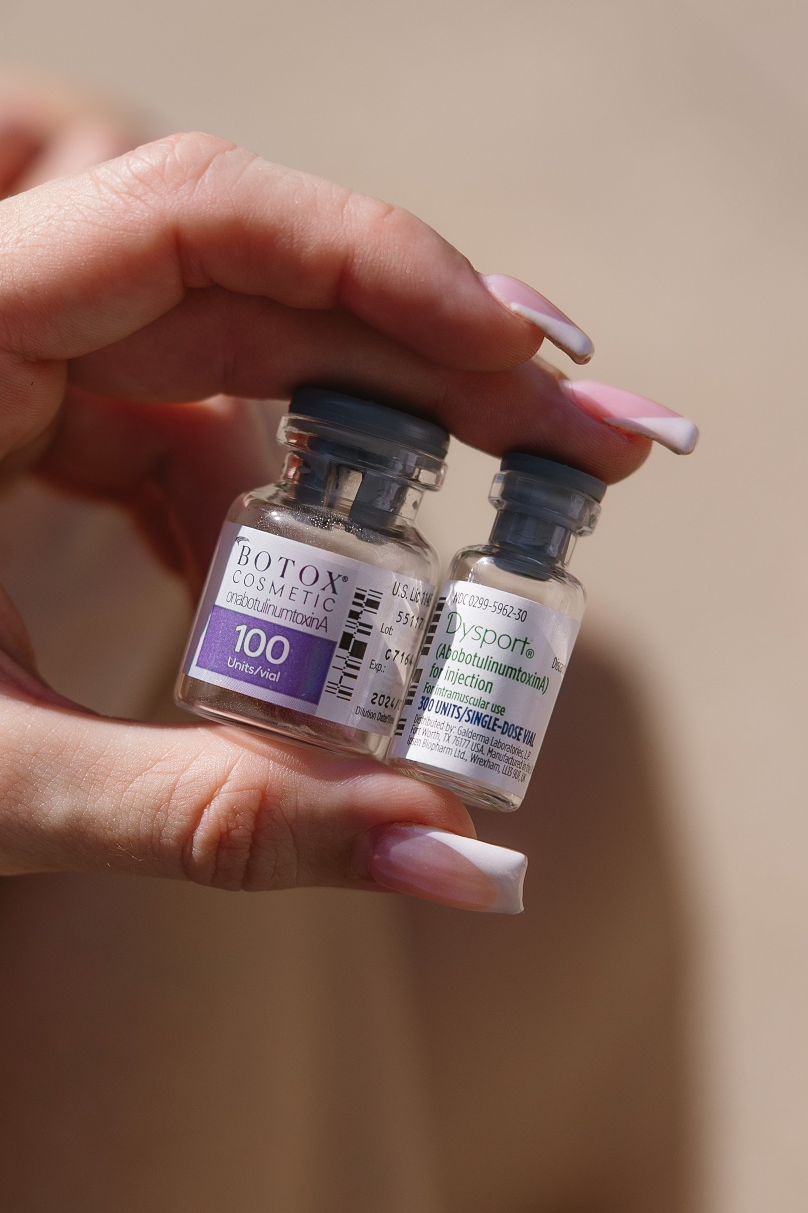 Hand holding two small medical vials labeled Botox and Dysport, both used for cosmetic or medical injections.