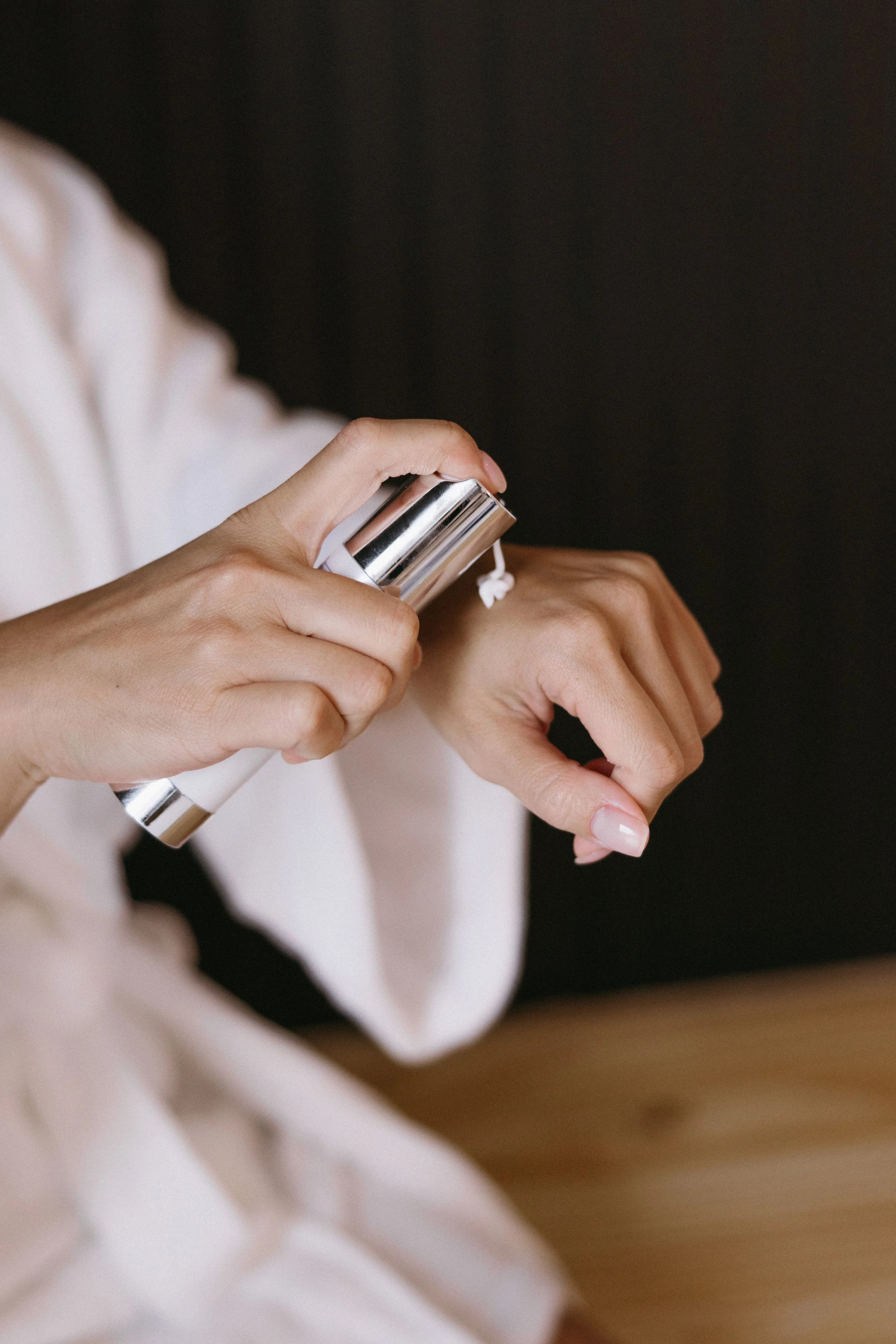 A person applying lotion or cream from a silver and white pump bottle onto their wrist.