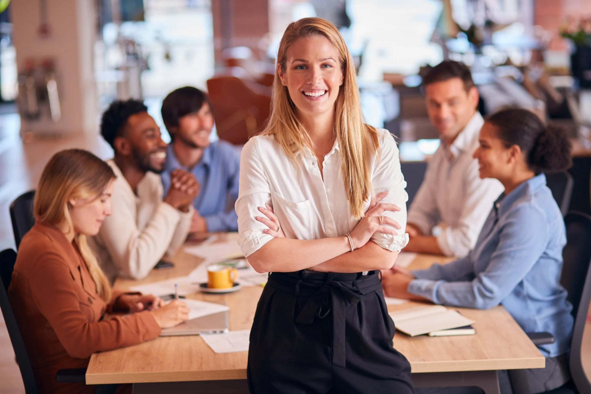 smiling woman standing in front of a table with other people sitting there.