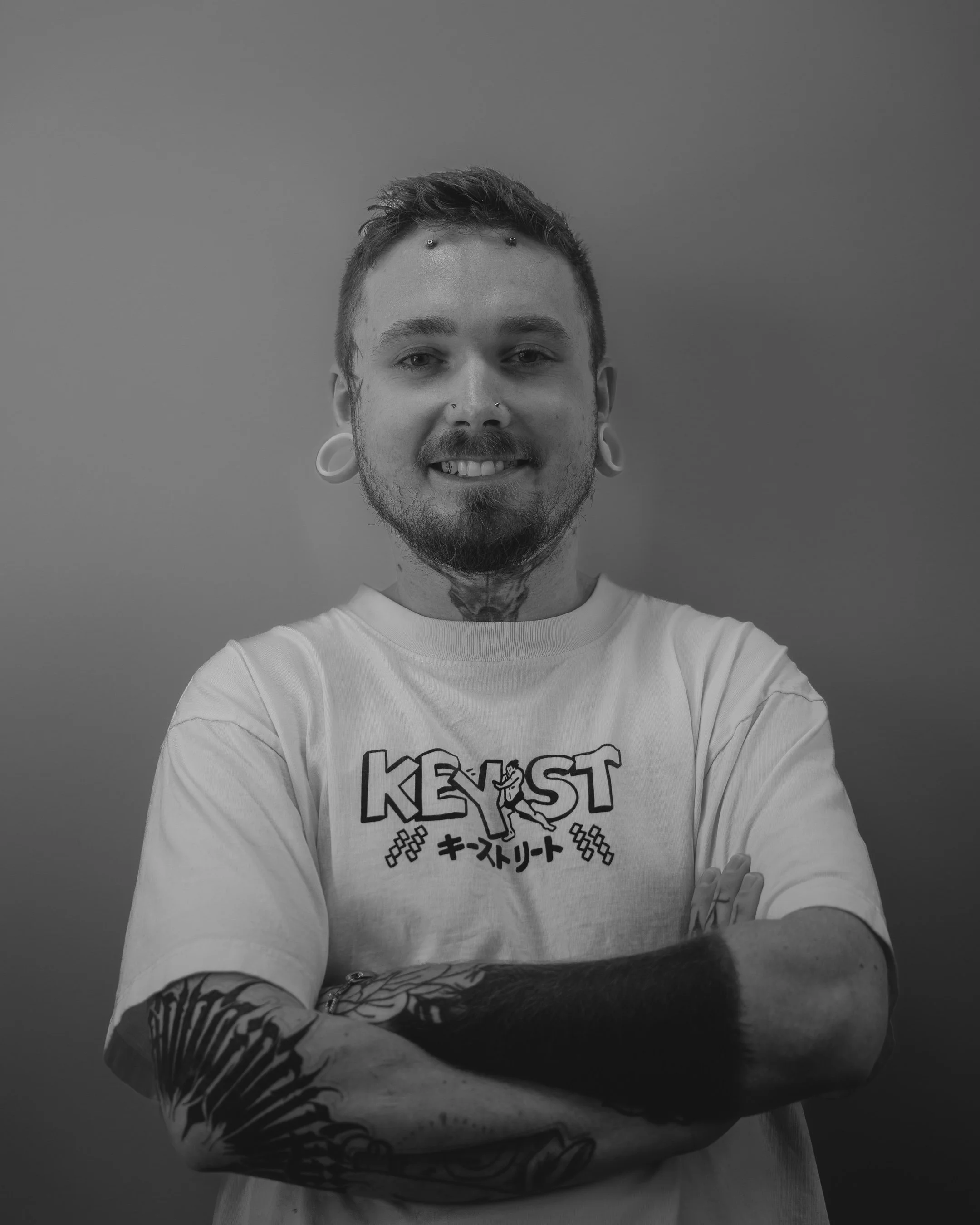 Person with glasses, tattoos, piercings, and black T-shirt smiling.