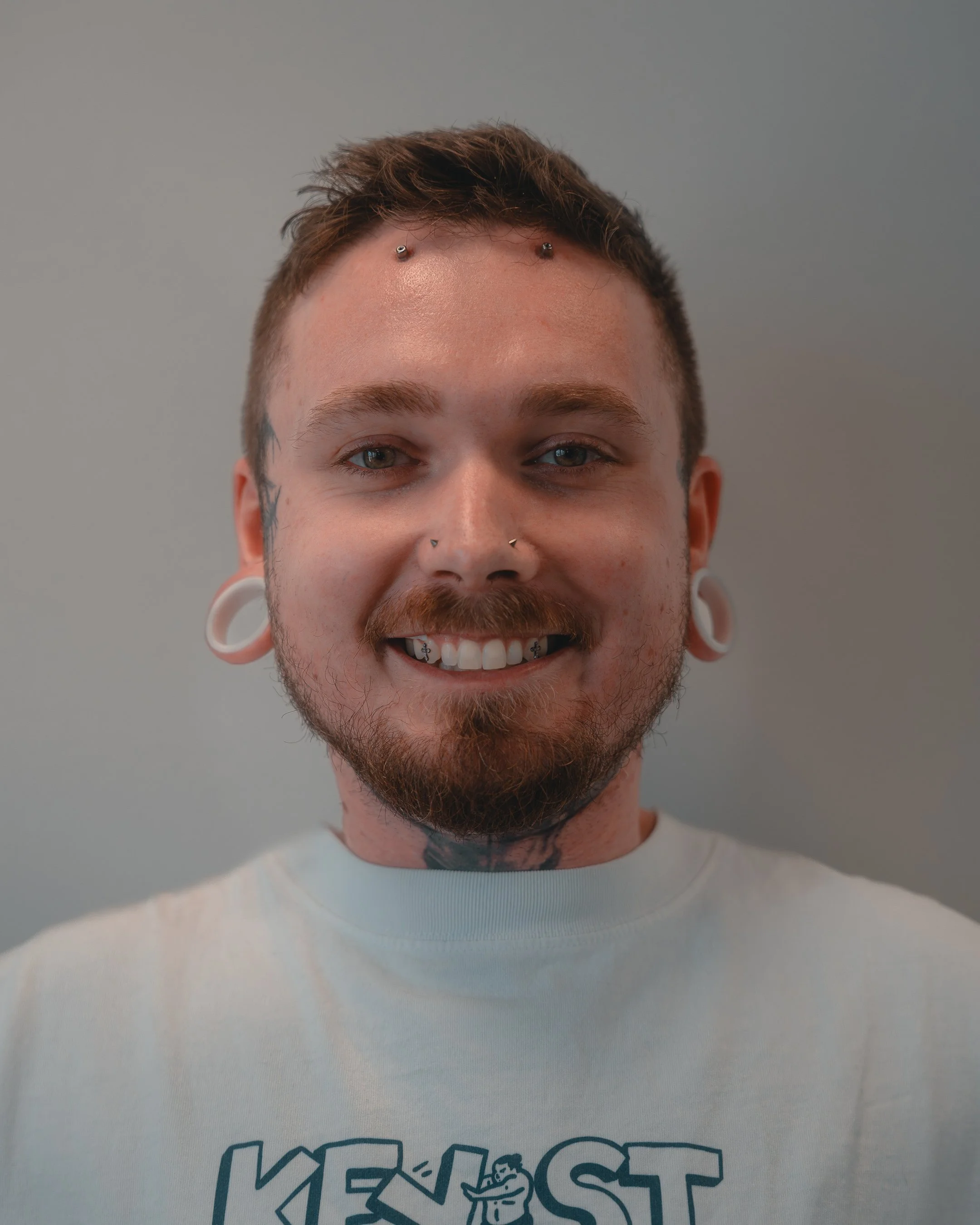 Person with glasses, tattoos, piercings, and black T-shirt smiling.