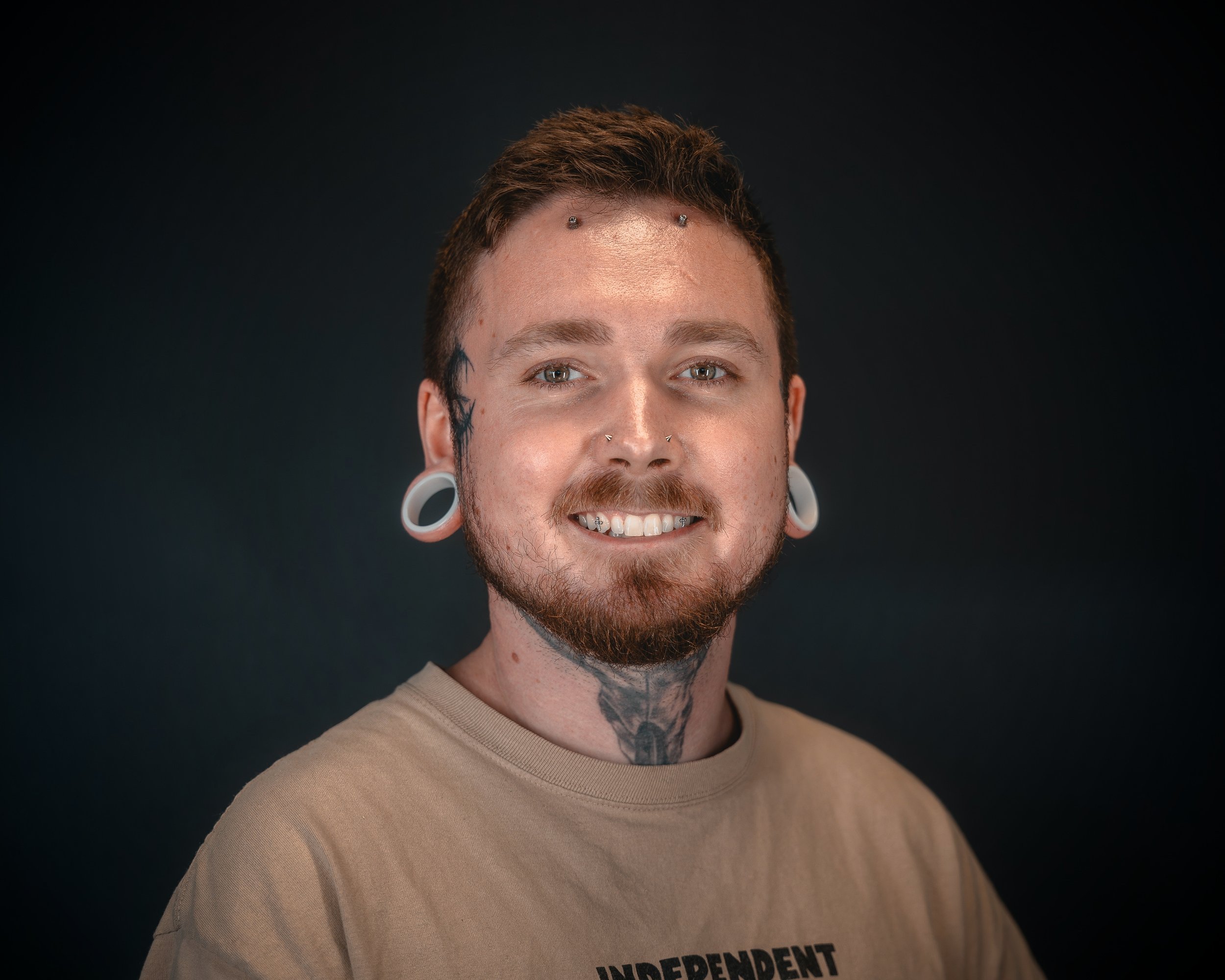 Person with tattoos, piercings, and black T-shirt smiling.