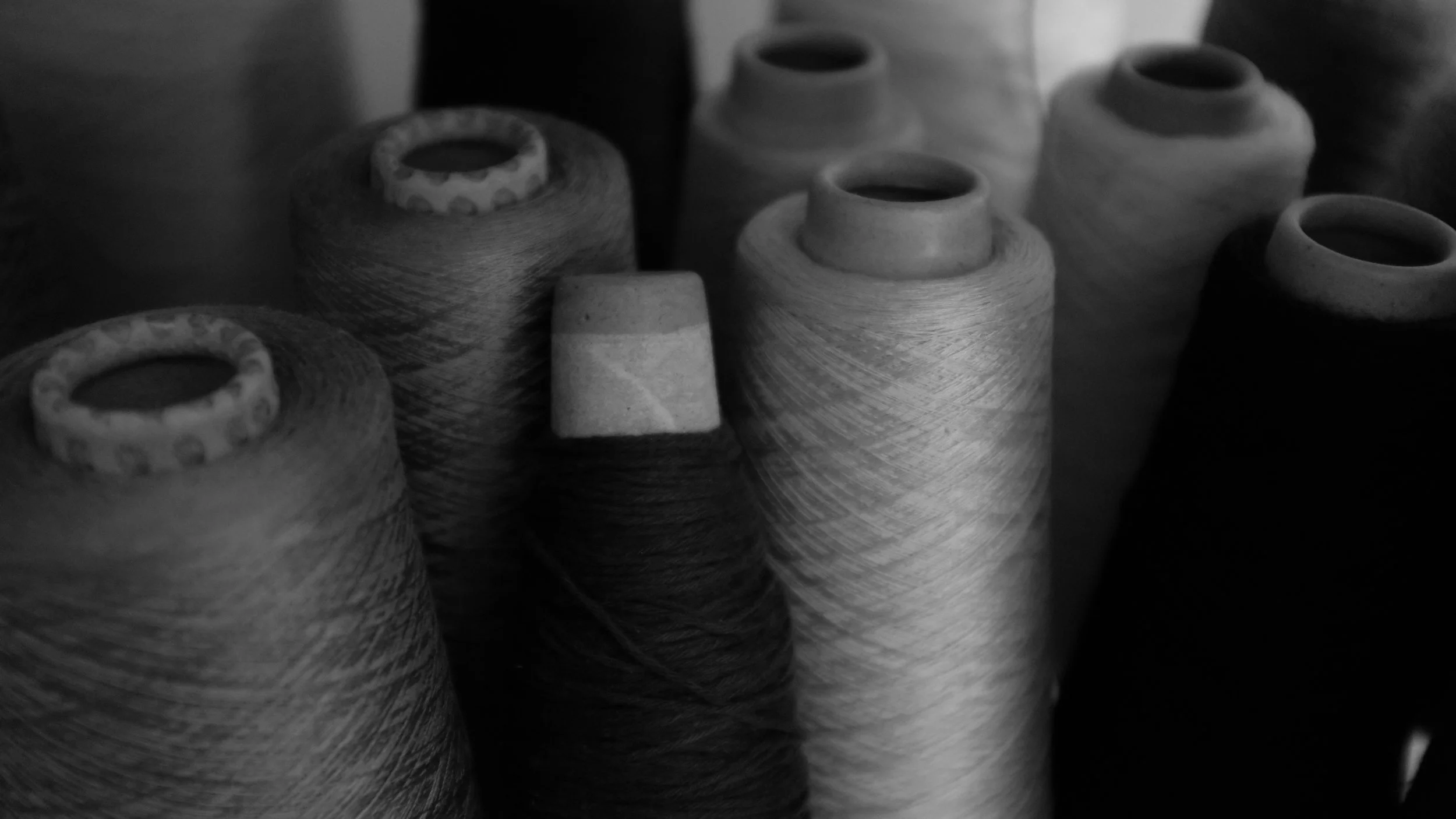 Close-up of multiple spools of thread or yarn in various shades, arranged vertically, with some spools partially overlapping each other.