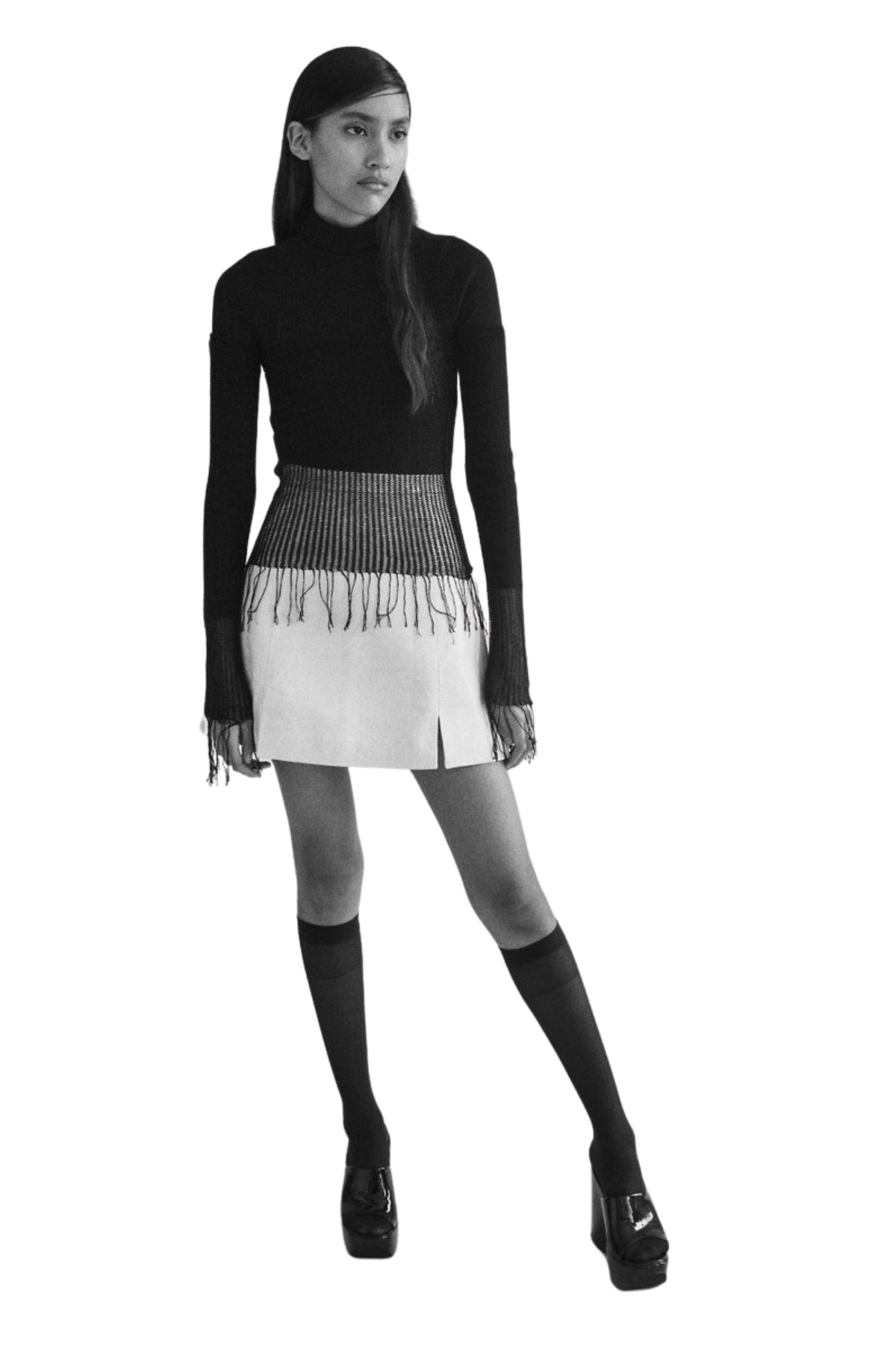 A woman in a black long-sleeve top, a striped high-waisted skirt with fringes, over-the-knee socks, and high heels.