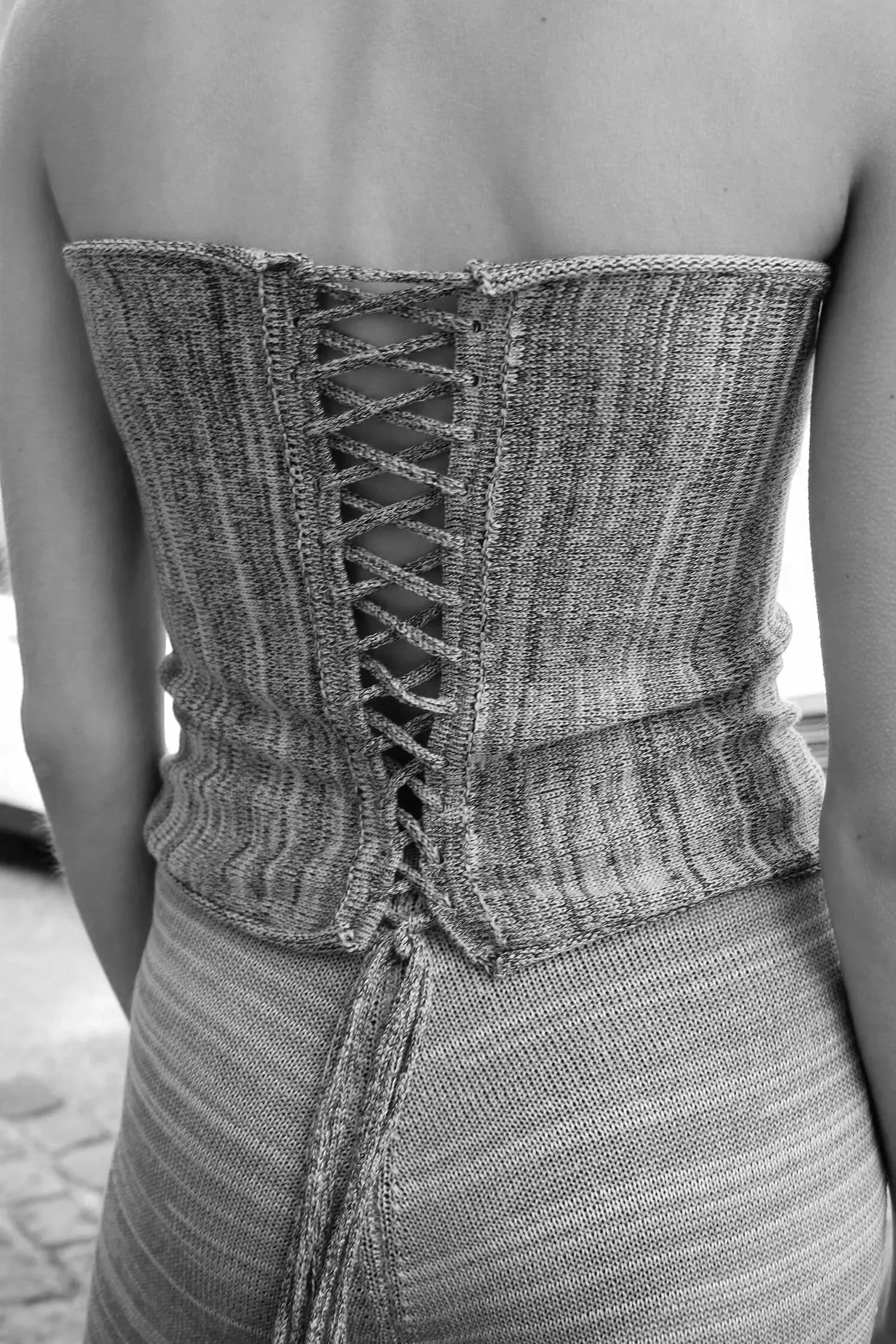 Back view of a person wearing a textured strapless top with a lace-up back and patterned high-waisted pants.