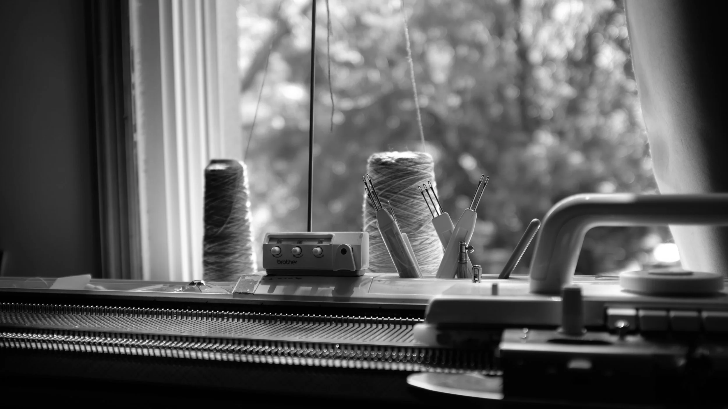 Sewing machine with spools of thread and sewing tool near a window in black and white.