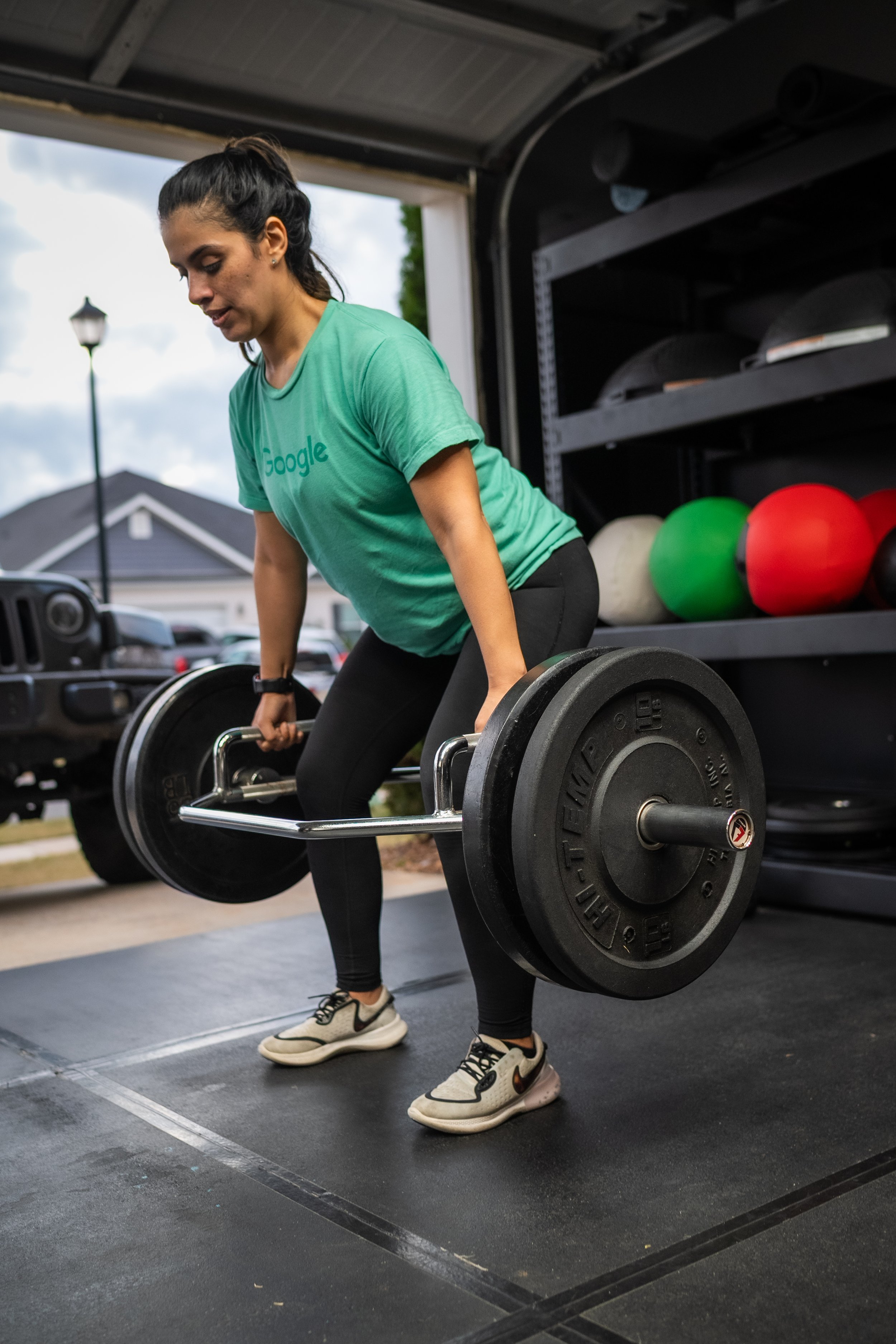 Woman in a green Google t-shirt lifting a barbell in a garage gym.