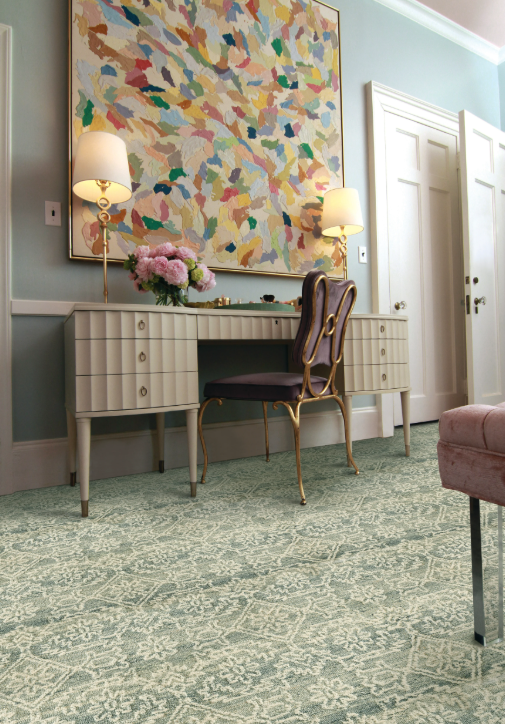 A study nook with an oversized abstract painting with a midcentury modern desk and chair underneath. Rosecore's Grandeur Lace in Ocean serves as a visual interest on the ground.