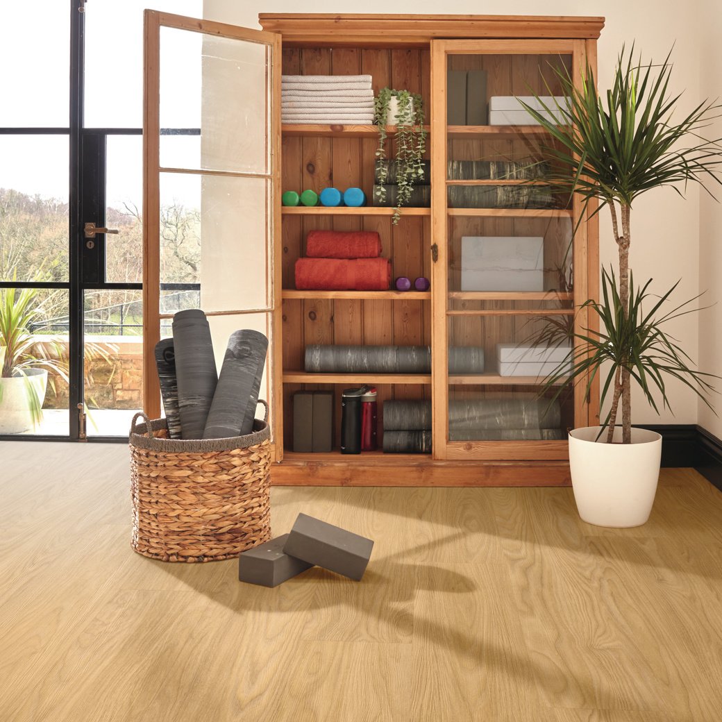 Warm colored wood workout cabinet with equipment with a palm tree and basket with yoga mats next to the cabinet. 