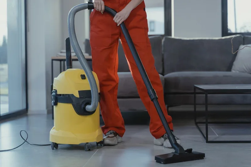 Woman vacuuming gray tile with yellow canister vacuum.