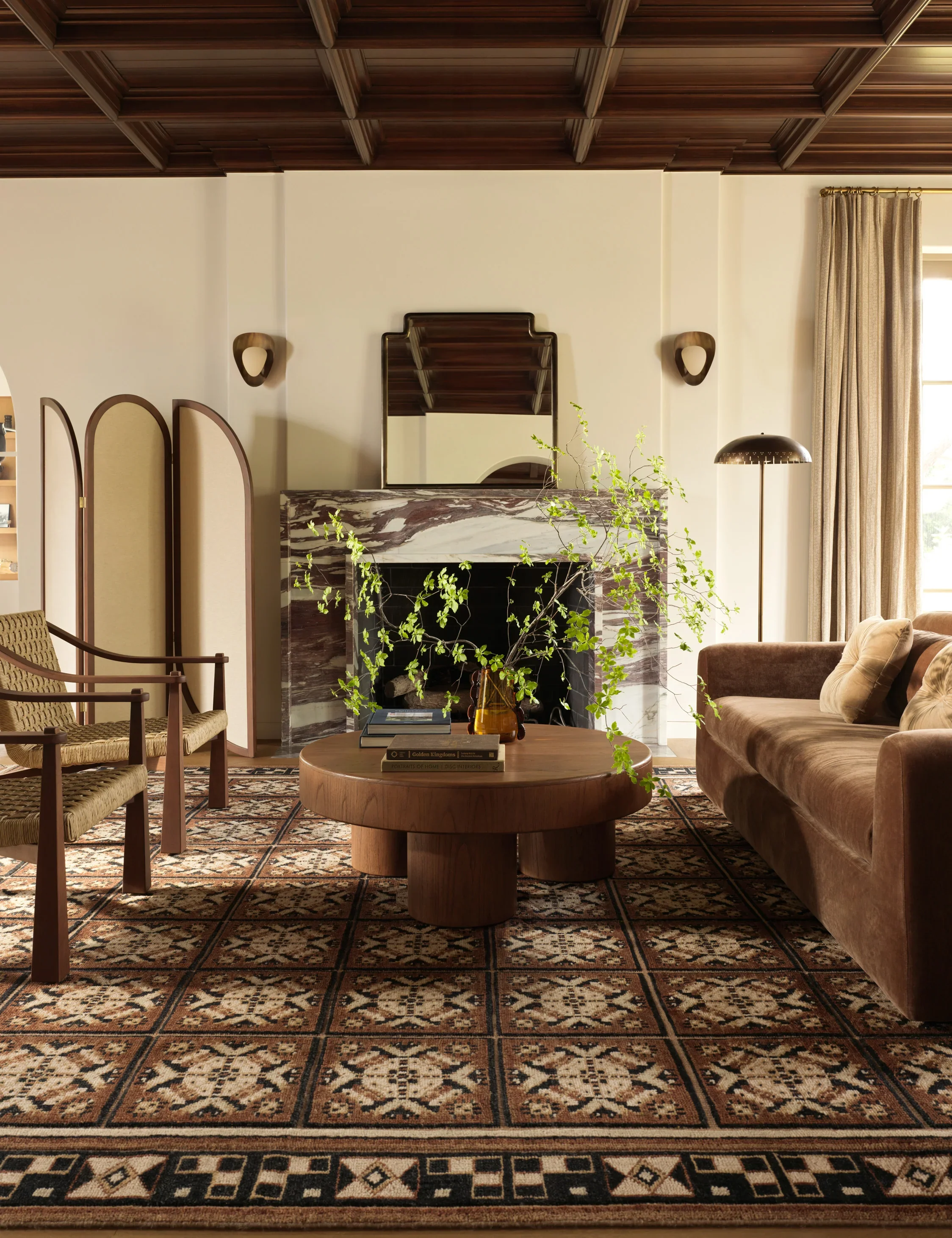 Modern living room with woven seats on chairs, a chunky wood coffee table, and a marbled stone fireplace hearth. A red and beige rug takes the vocal point on the ground
