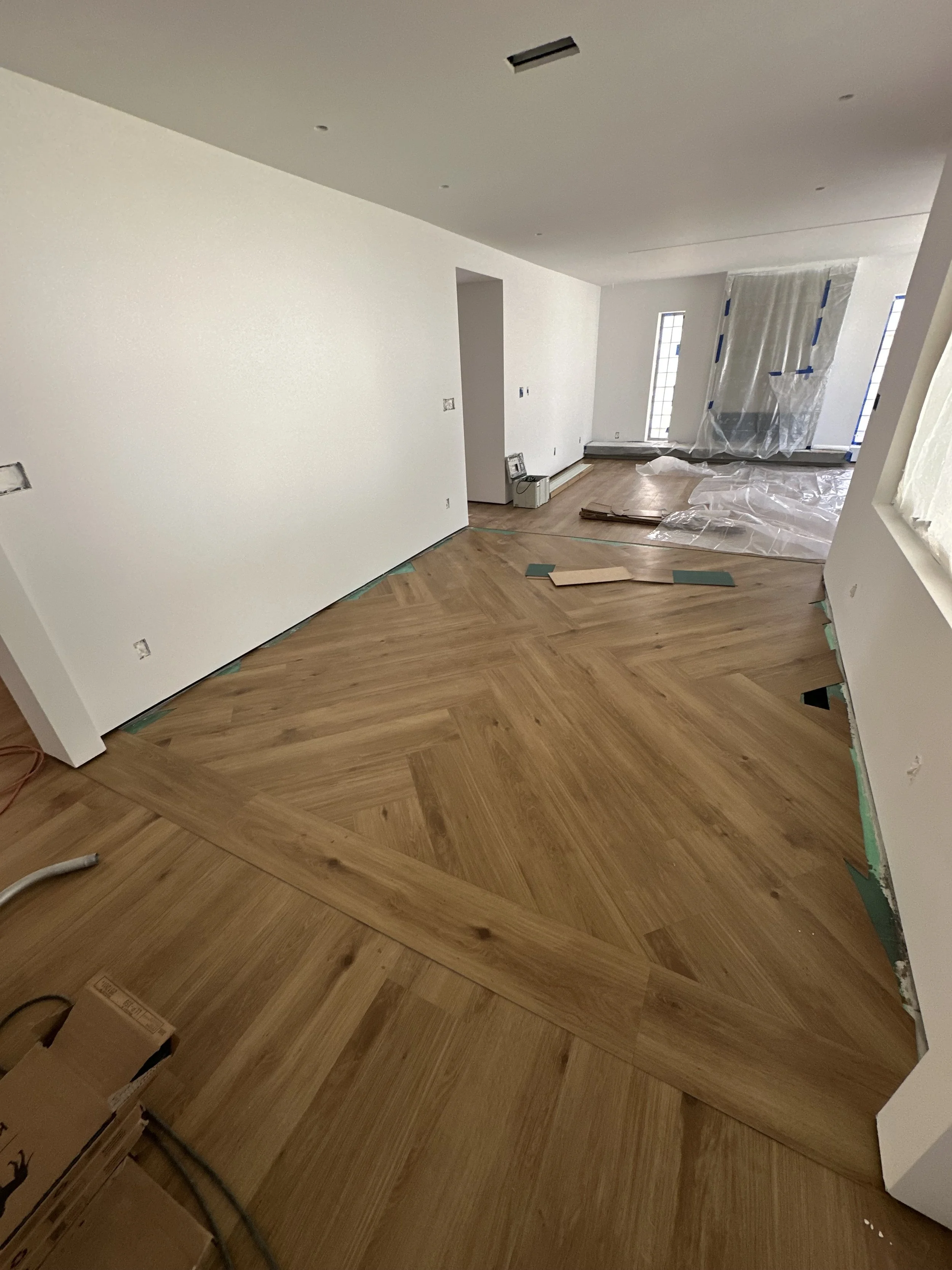 A large hallway with a herringbone-x pattern on the floor in the middle of being installed.