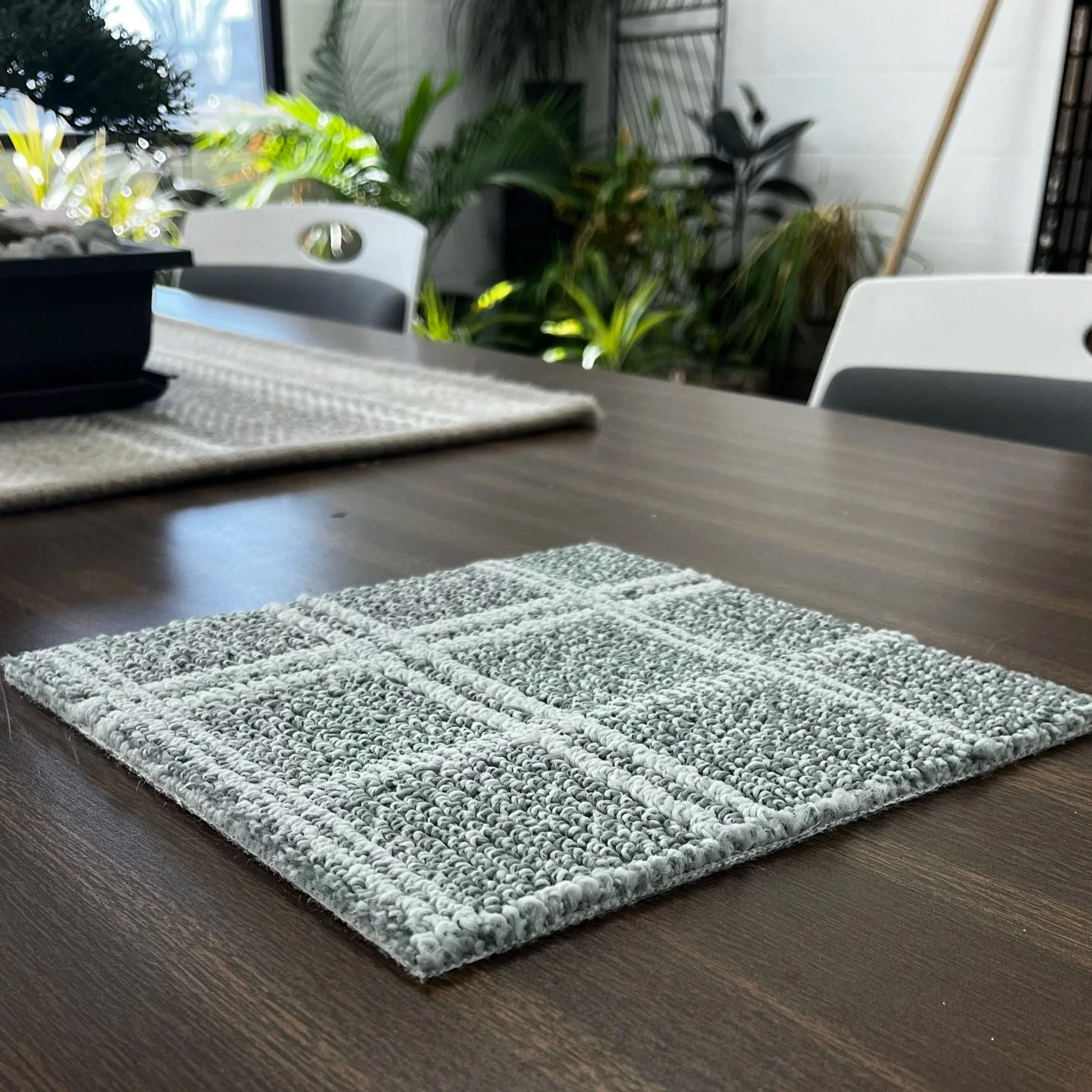 A sample of Anderson Tuftex's Breeze Block in Blue Fern on a table with a plant garden in the background