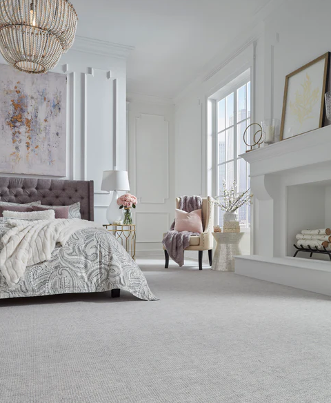 A clean bedroom with minimal colors. The bedrame is purple, and there are mathcing purple blankets and pillows placed throughout the room. An abstract painging hanging over the bead. Masland's Hera in Child carpet adds a soft touch.