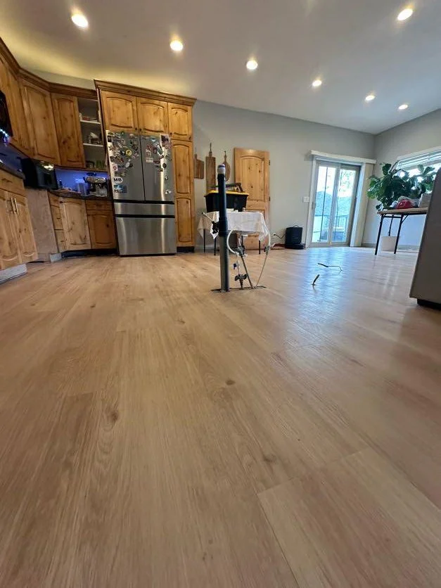 Empty kitchen and dining area with wooden cabinets, stainless steel refrigerator, sliding glass door, and hardwood floor, with a plumbing fixture and tools in the center of the room.