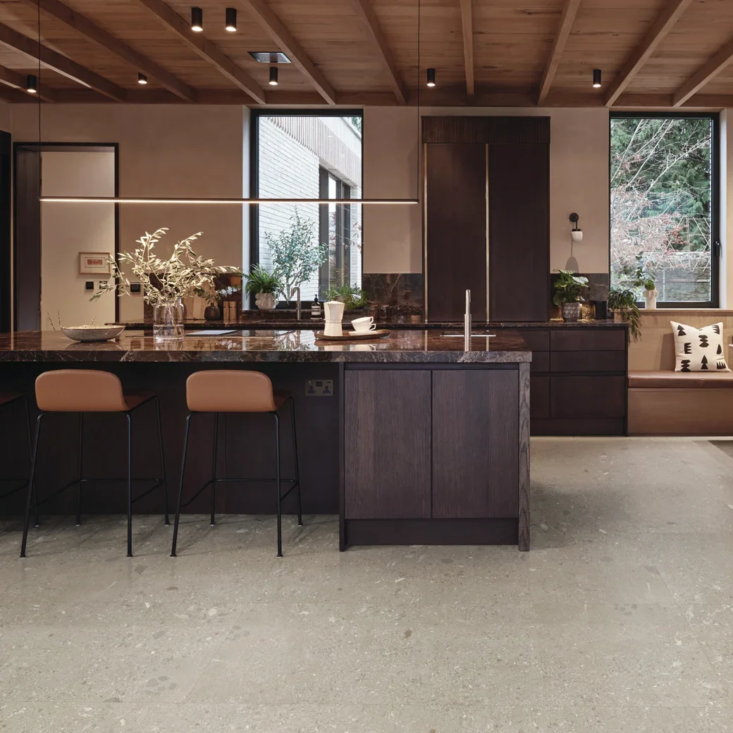A sleek, modern kitchen with dark cabinets and countertops, a wood planked ceiling, and an island seating area.