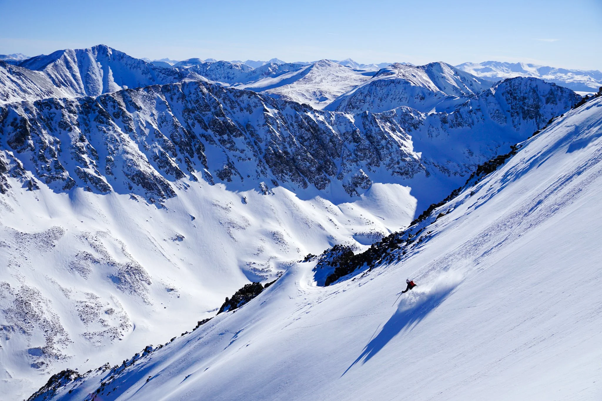 male skier wearing a red backpack skiing down powder in the Colorado Rocky Mountains