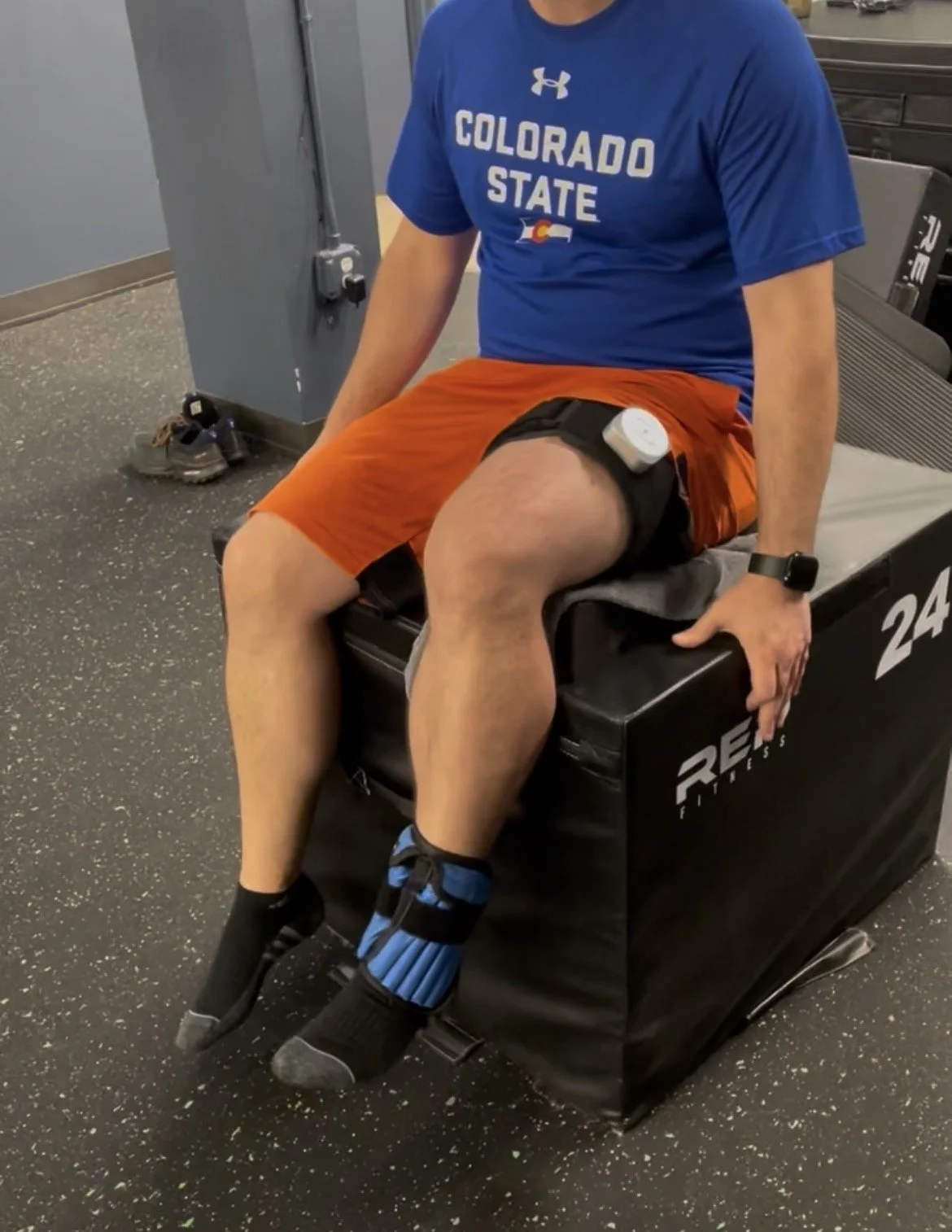 male athlete in a colorado state tshirt, rehabbing from a knee injury using blood flow restriction therapy to maintain and build strength