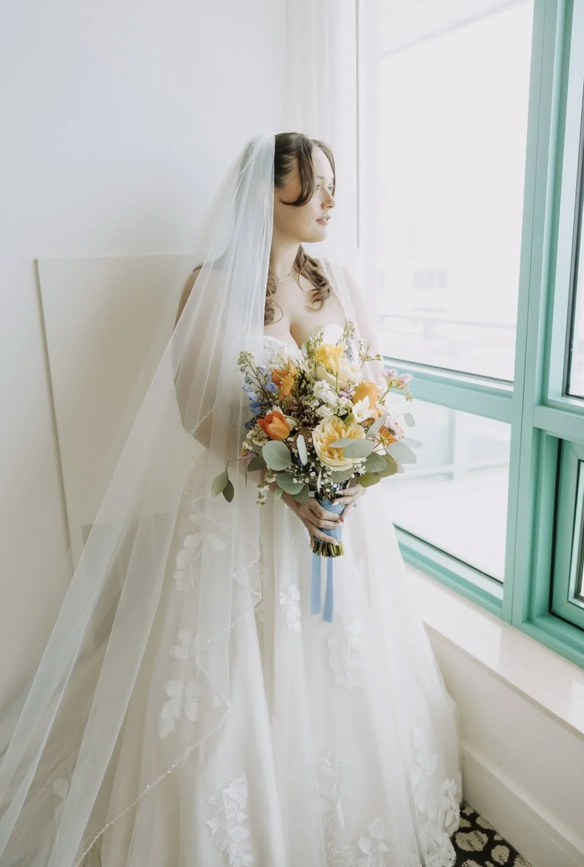 A bride looking out the window holding a bouquet.