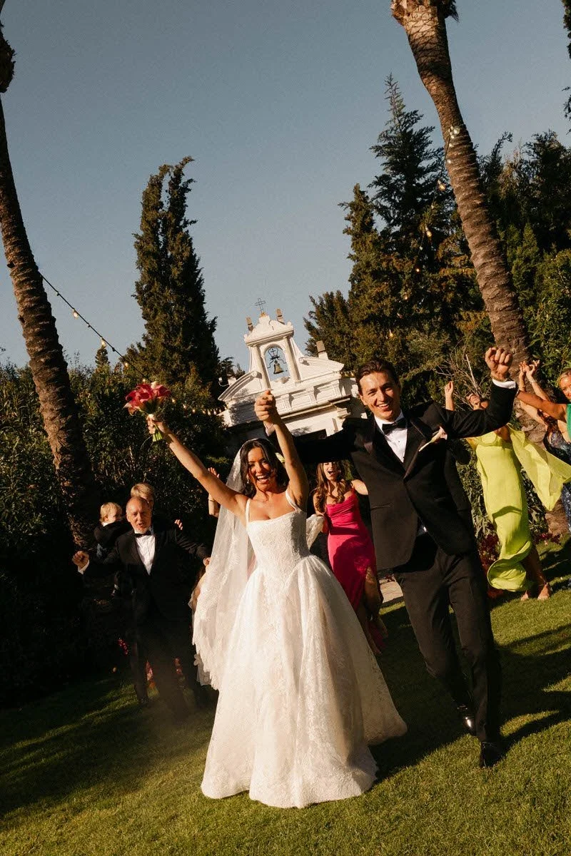 A couple just married happily lifting their arms up outside.