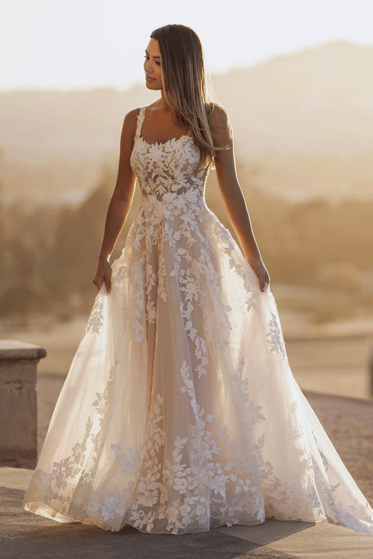 A woman in a white lace bridal gown standing outdoors at sunset with mountains in the background.