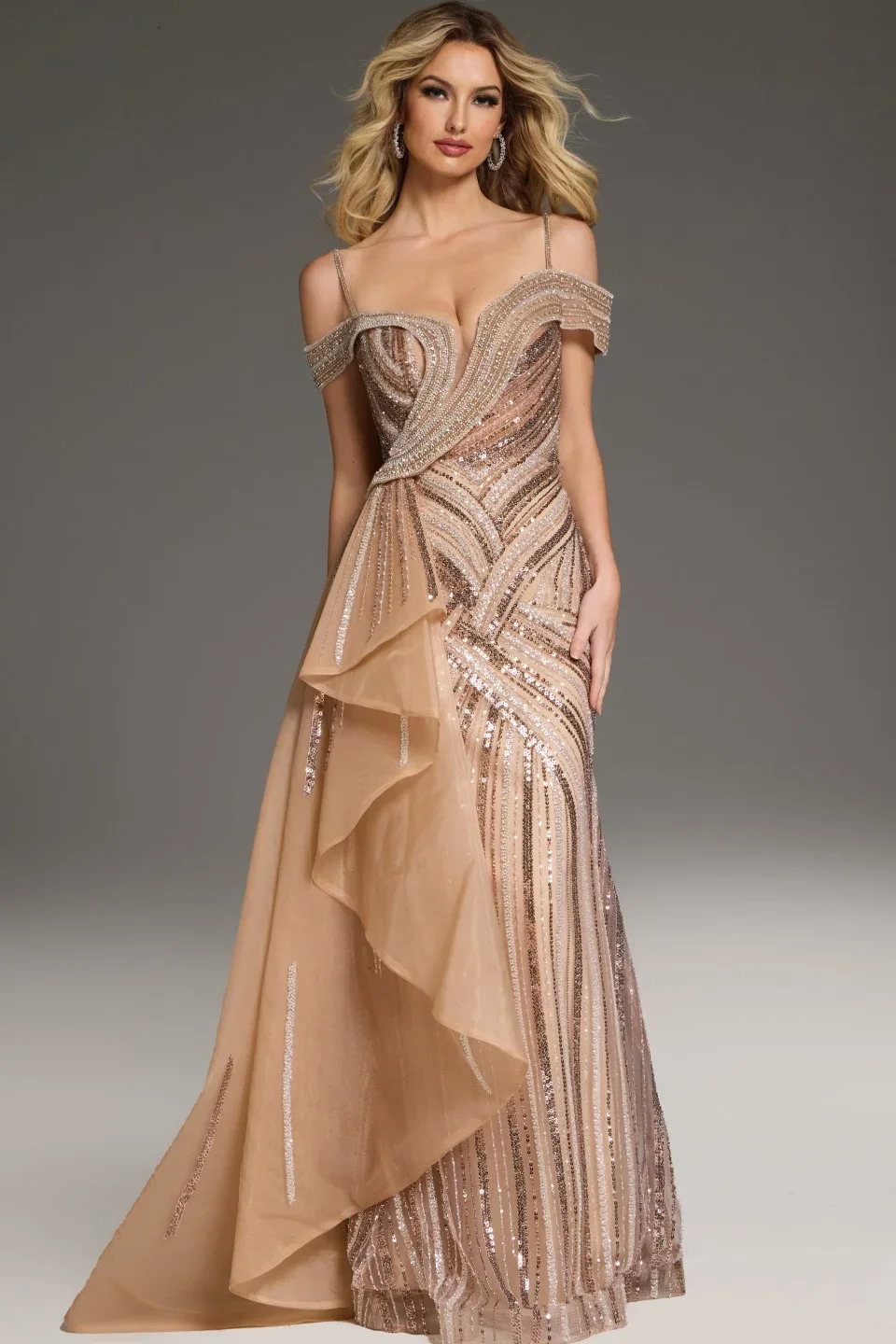 A woman wearing an elegant, rose gold evening gown with intricate beading and sequins, featuring a fitted bodice, off-the-shoulder straps, and a layered ruffle detail on the skirt, standing against a plain gray background.