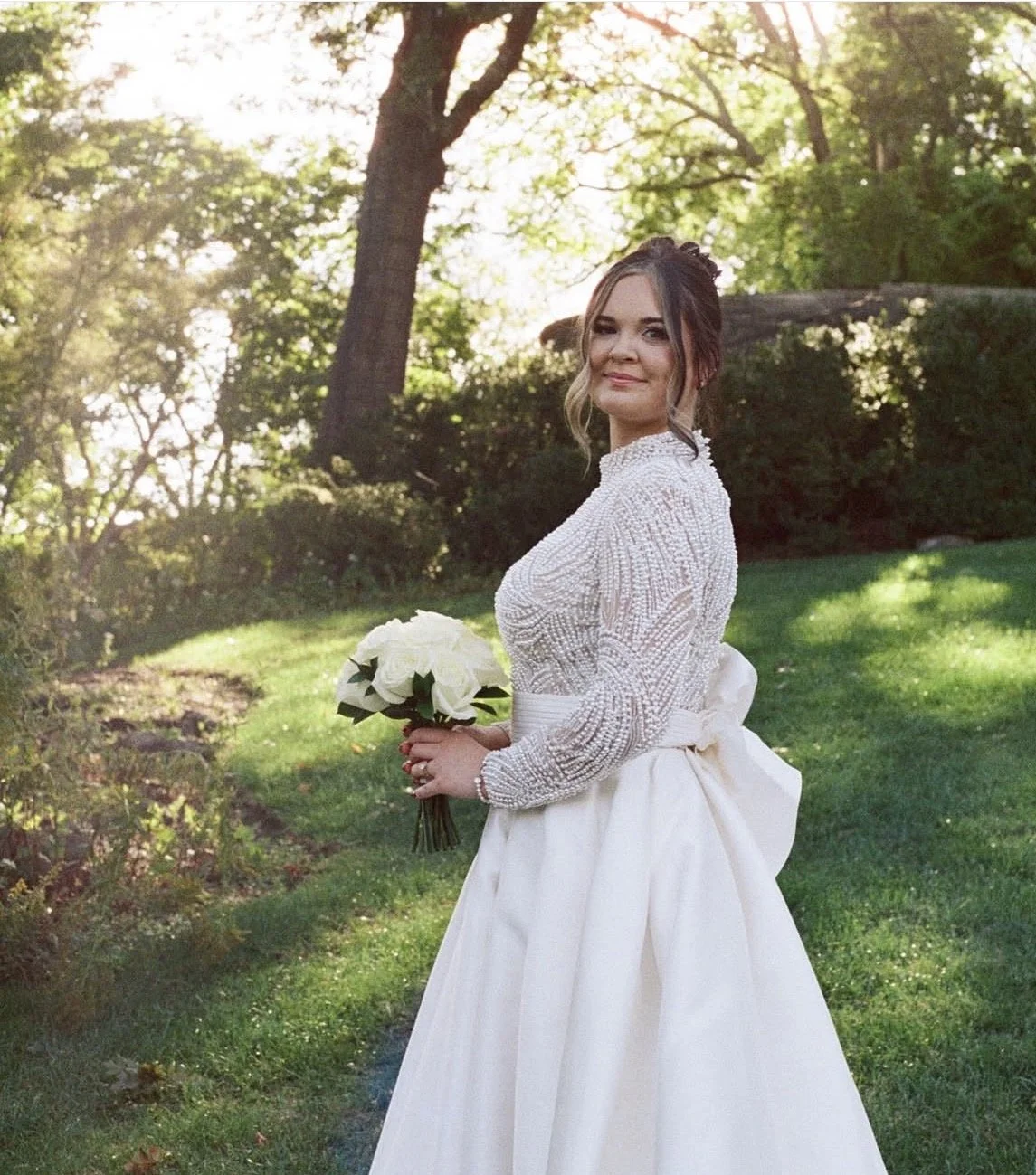 A bride holding a bouquet standing in front of trees. 