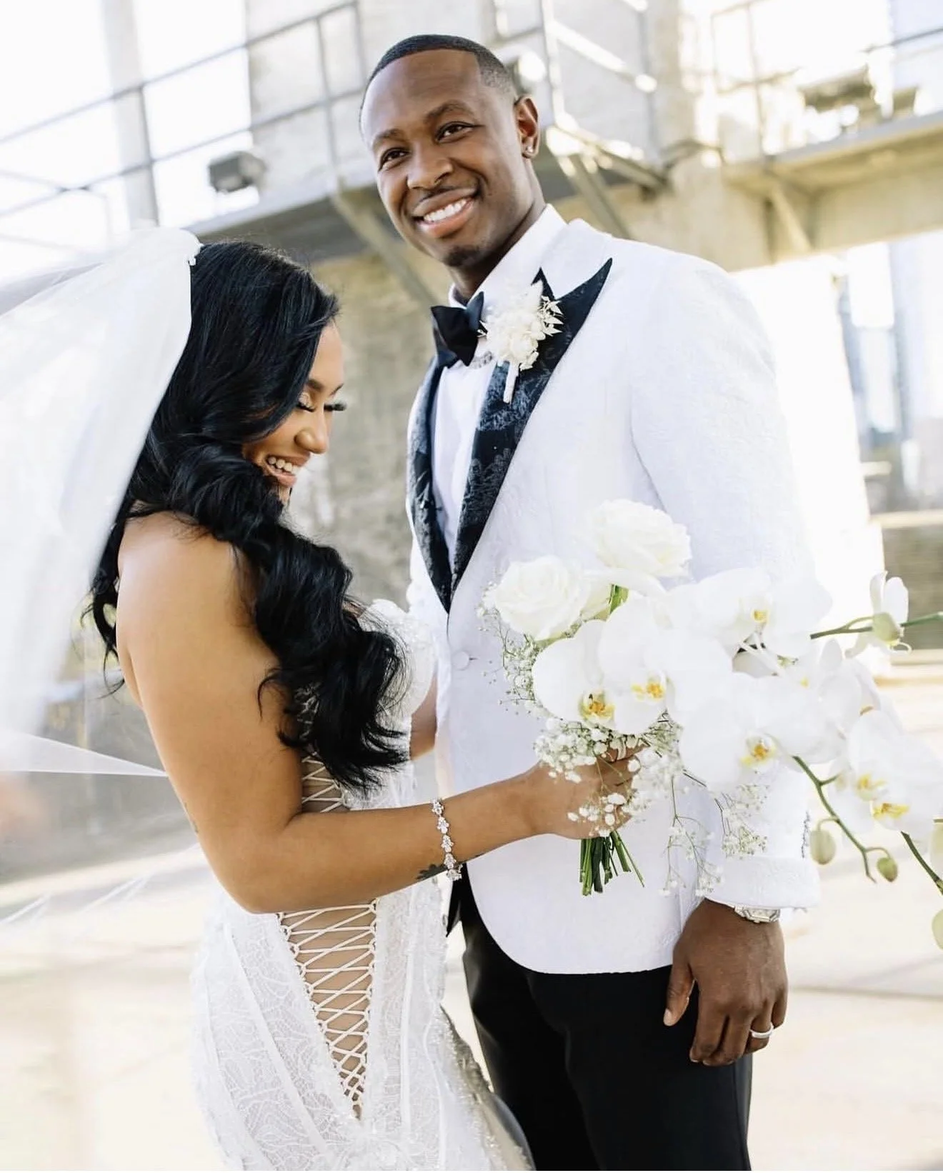A bride and groom on their wedding day smiling outside. The bride is holding a bouquet.