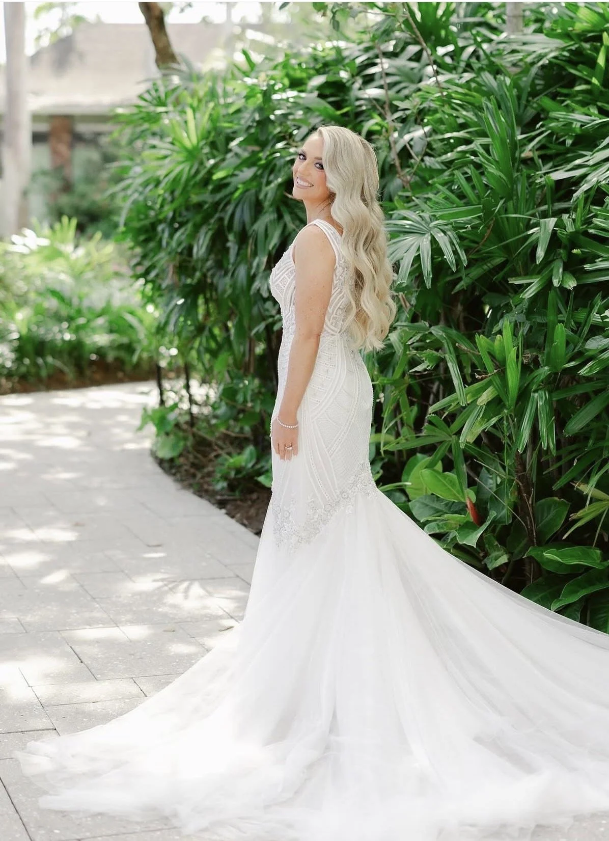 A bride in front of greenery looking back over her shoulder.
