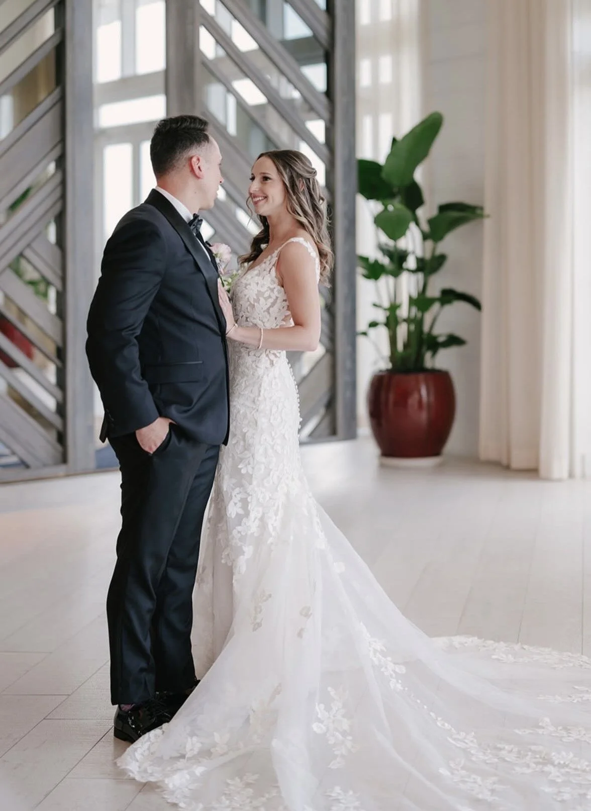 A couple on their wedding day smiling at each other indoors.