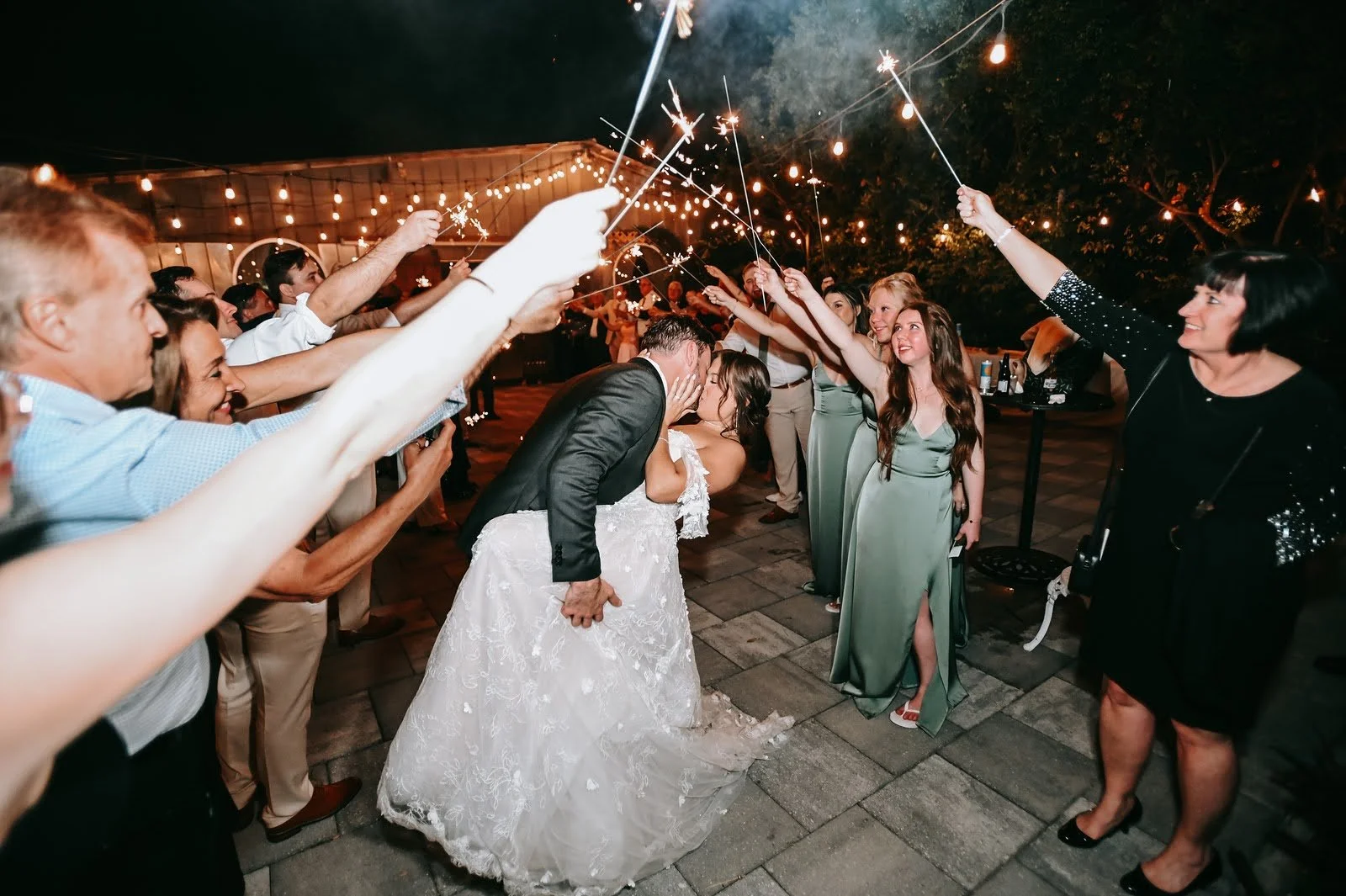 A bride and groom kissing outside as their guests hold sparklers above them.