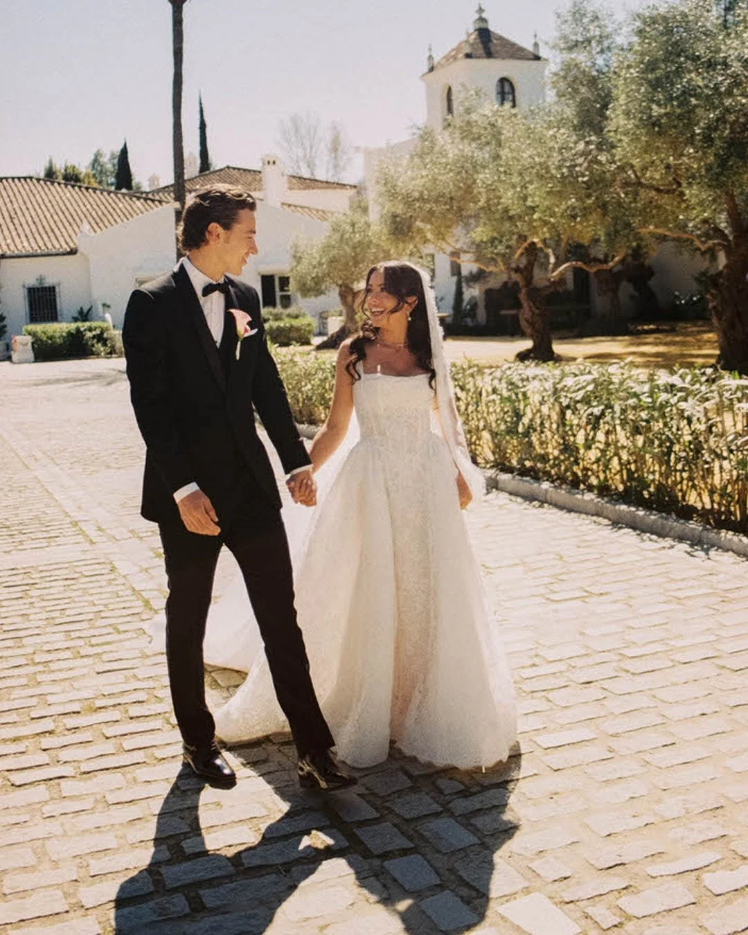 A couple outside on their wedding day holding hands and smiling at each other.