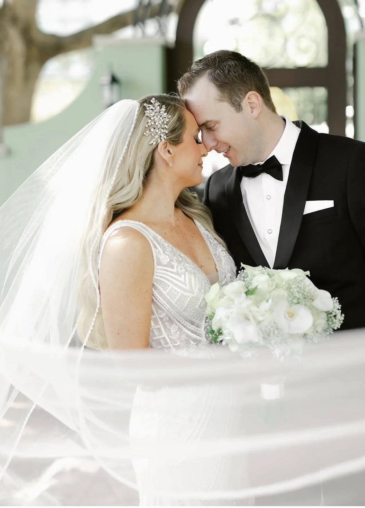 A newlywed couple posed closely together with the bride holding her bouquet.