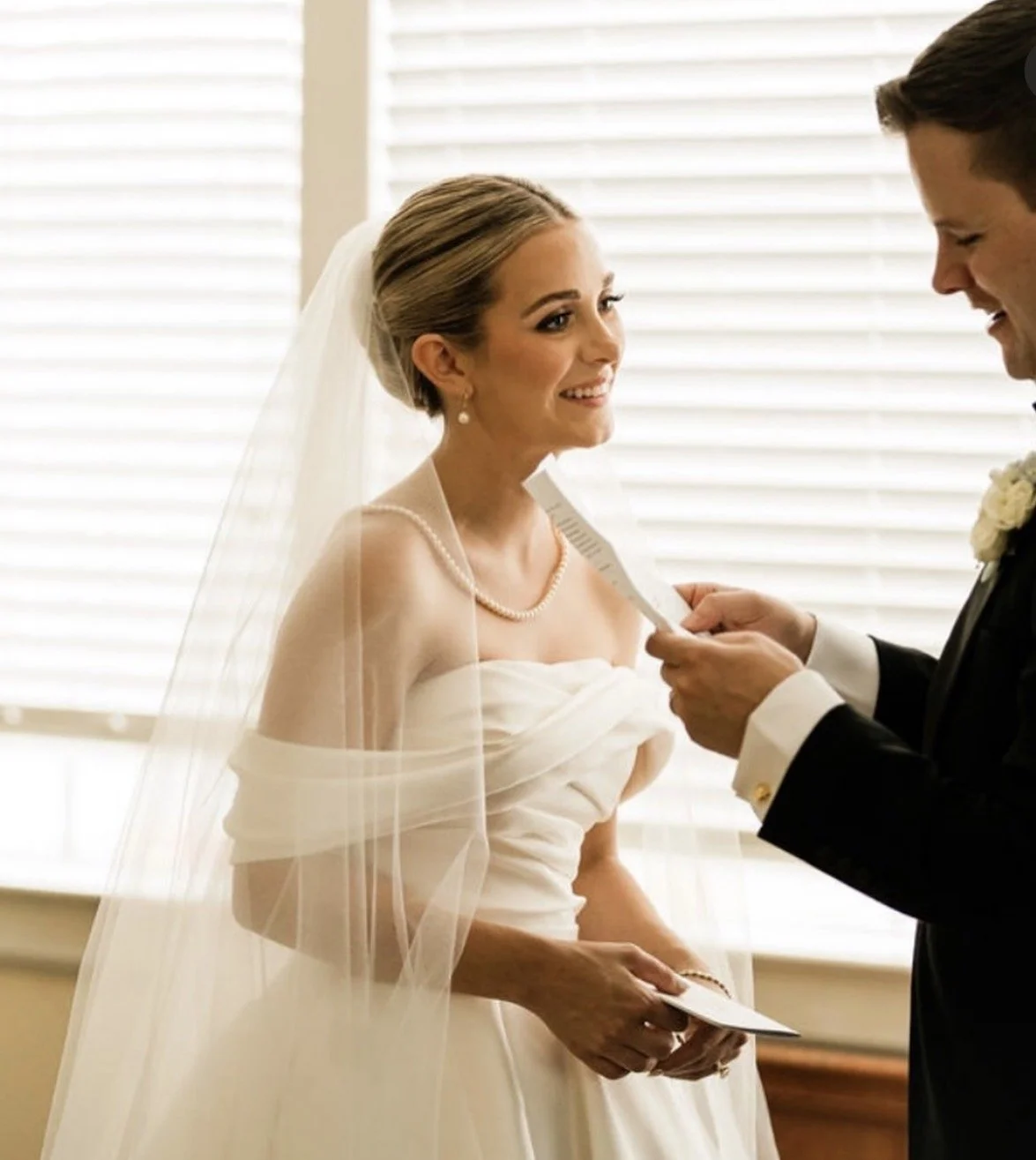 A groom off to the side reads his vows while his bride centered in the photo smiles at him.