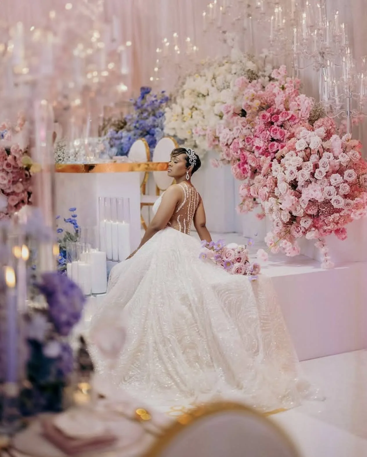 A bride sitting inside in front of flowers and candles.
