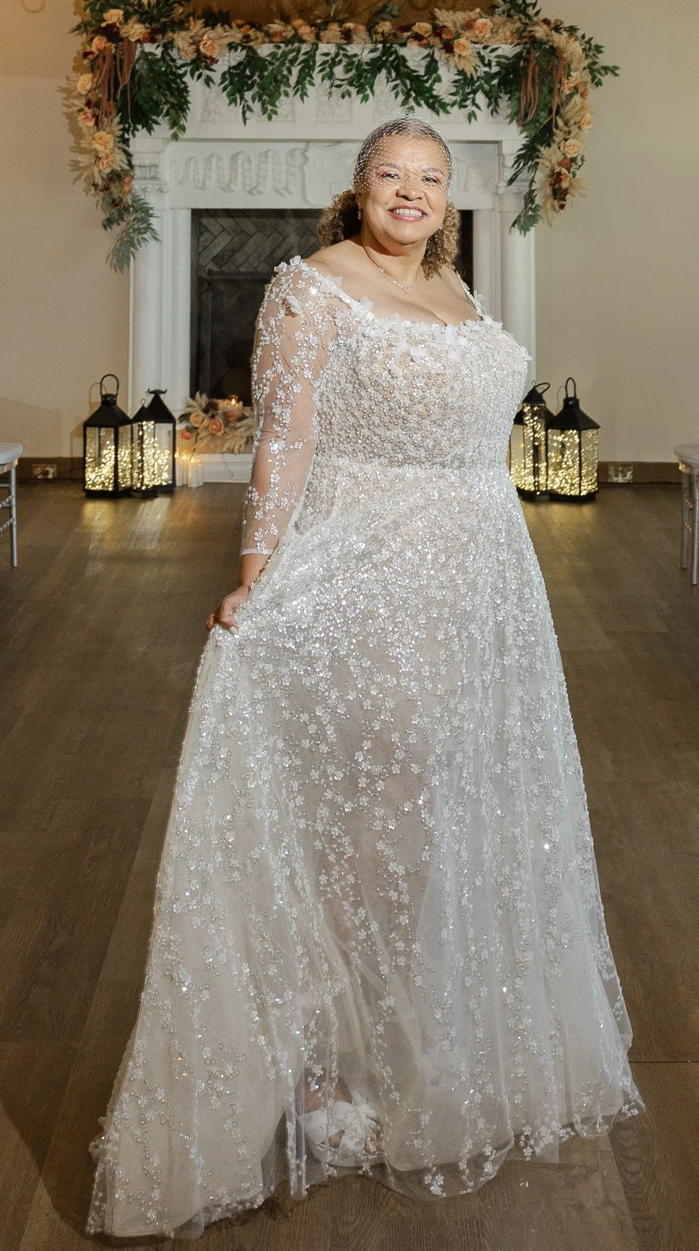 A bride in front of a fireplace with flowers above it.
