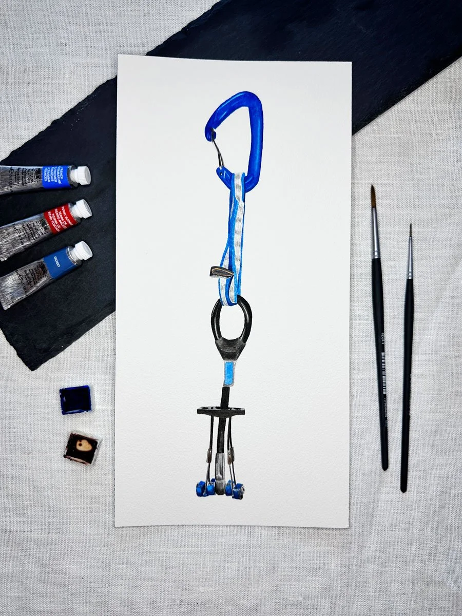 A watercolor painting of a scooter with a blue carabiner at the top, set on a white canvas surrounded by art supplies including paint tubes, brushes, and paint palettes.