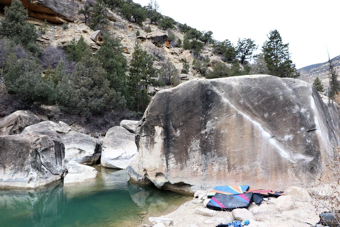 photograph of a rock climbing boulder on a creek with crash pads in the foreground