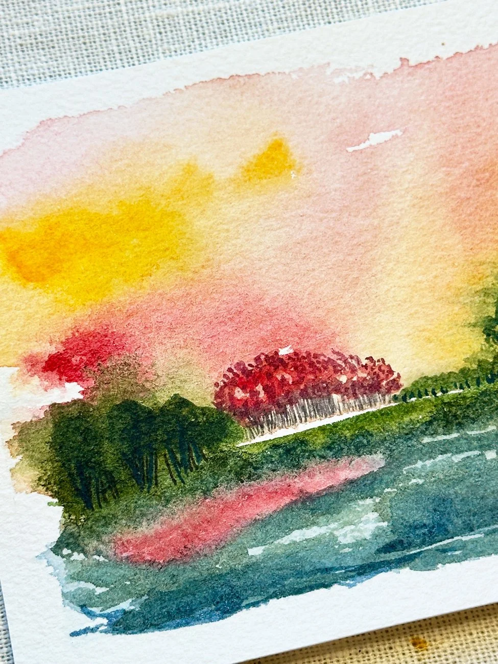 Watercolor painting of a landscape with trees, a pathway, a body of water, and a colorful sky with pink, orange, and yellow hues.